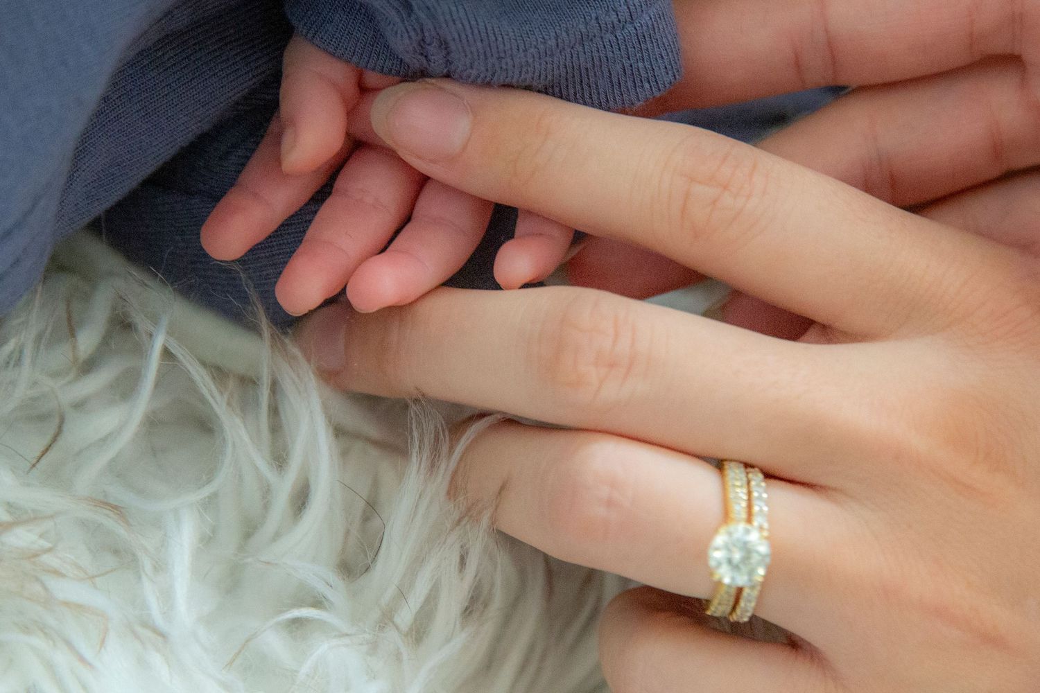 Close up of mom and newborn hand with engagement ring and wedding band.