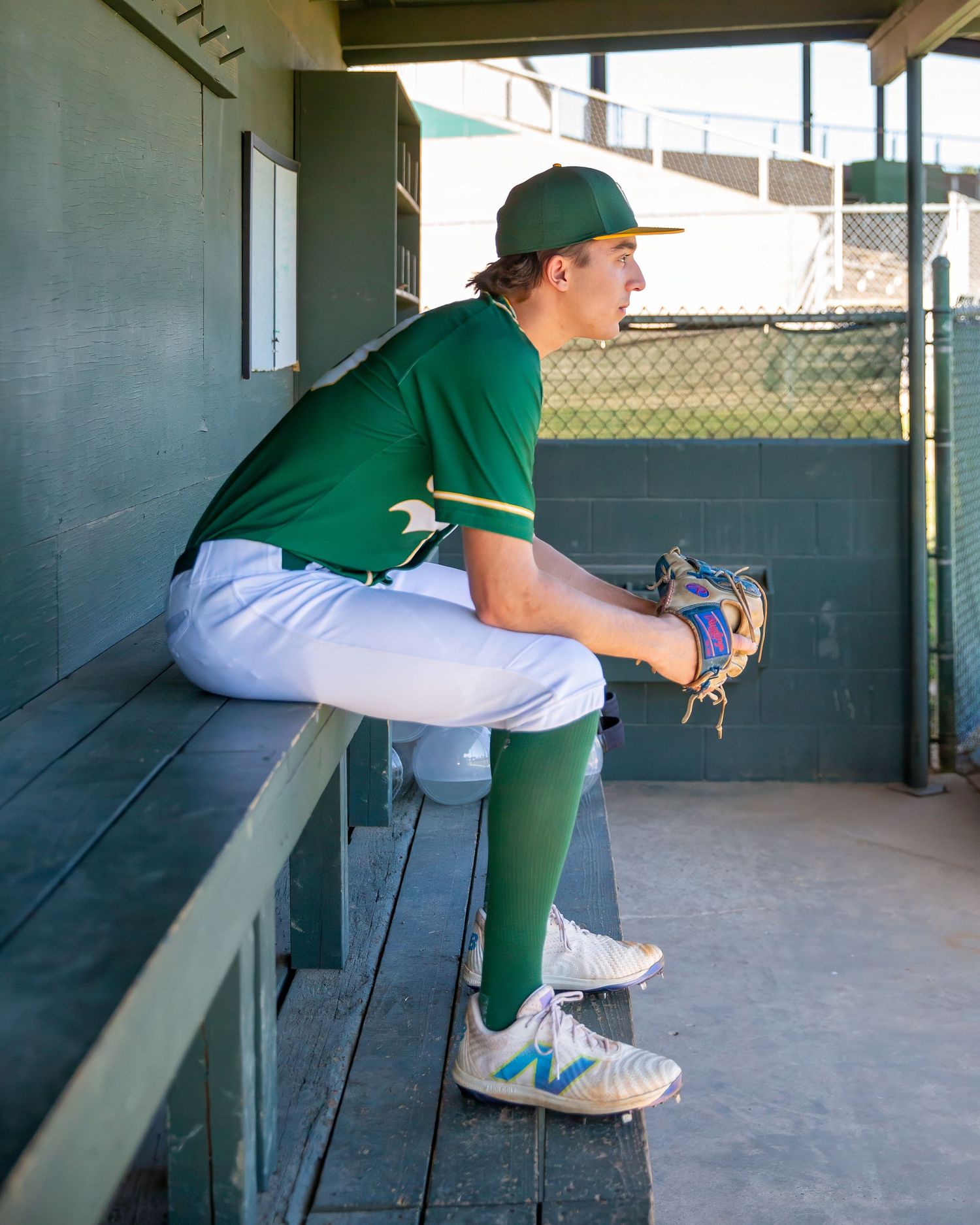 Baseball player in green uniform sitting in dugout shown from multiple angles.