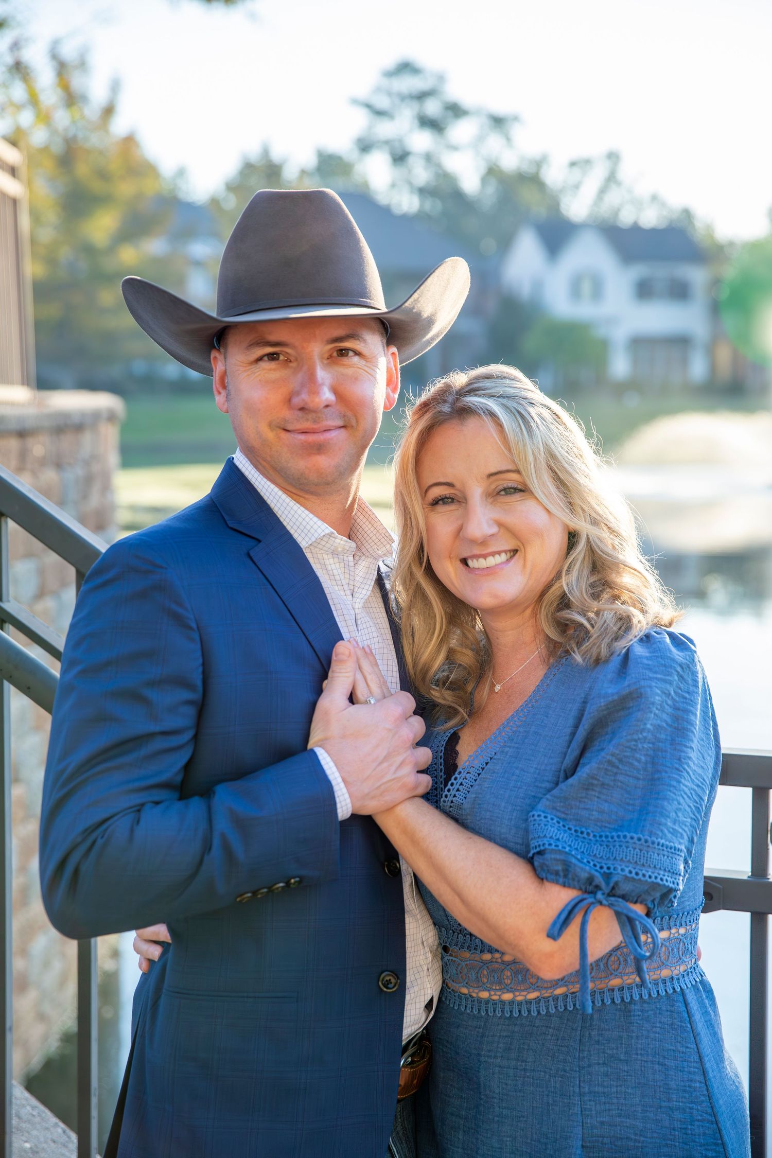 Romantic couple in western attire posing together by waterfront during golden hour.