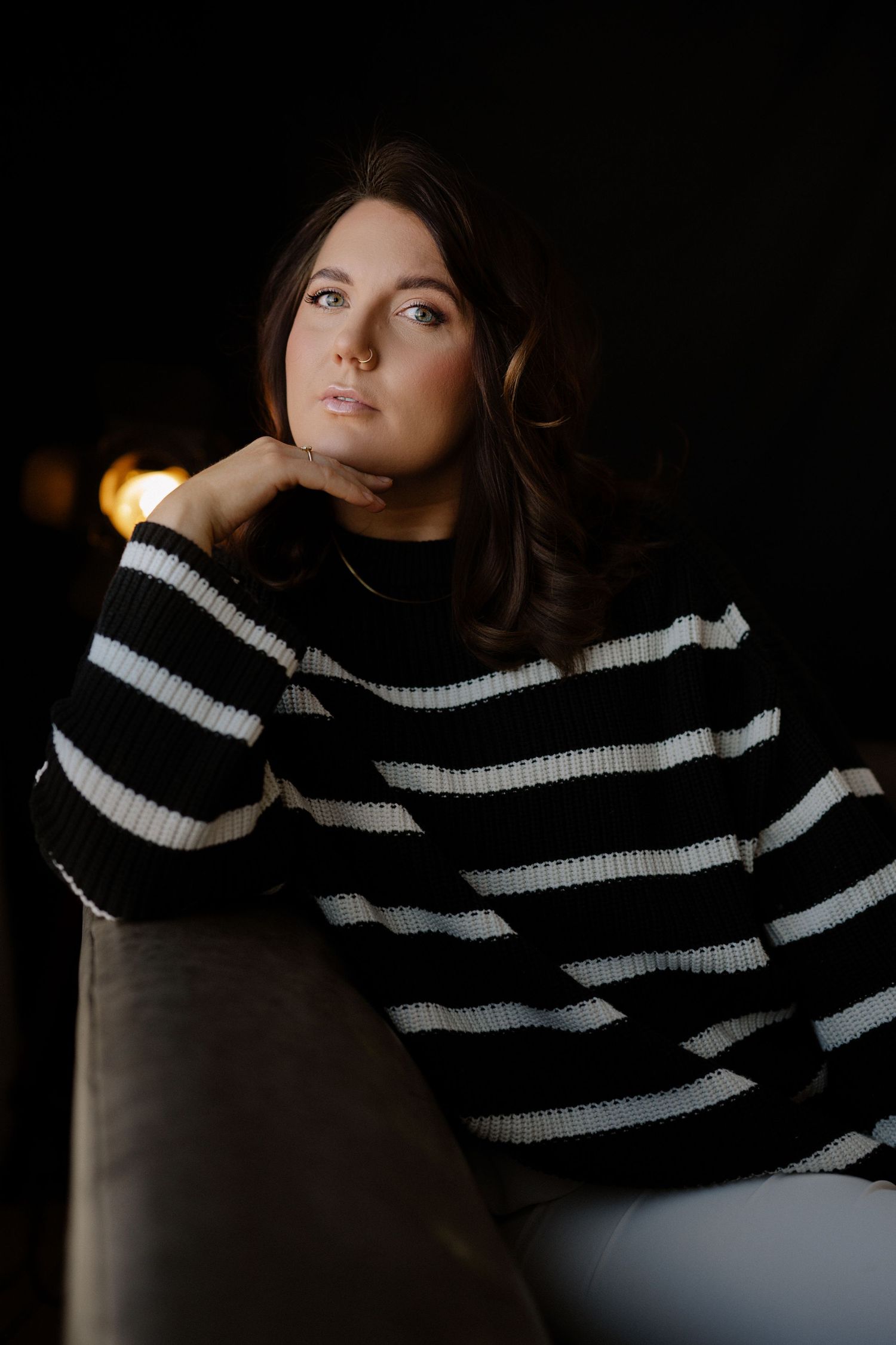 Portrait of woman in striped sweater posing thoughtfully against dark background.