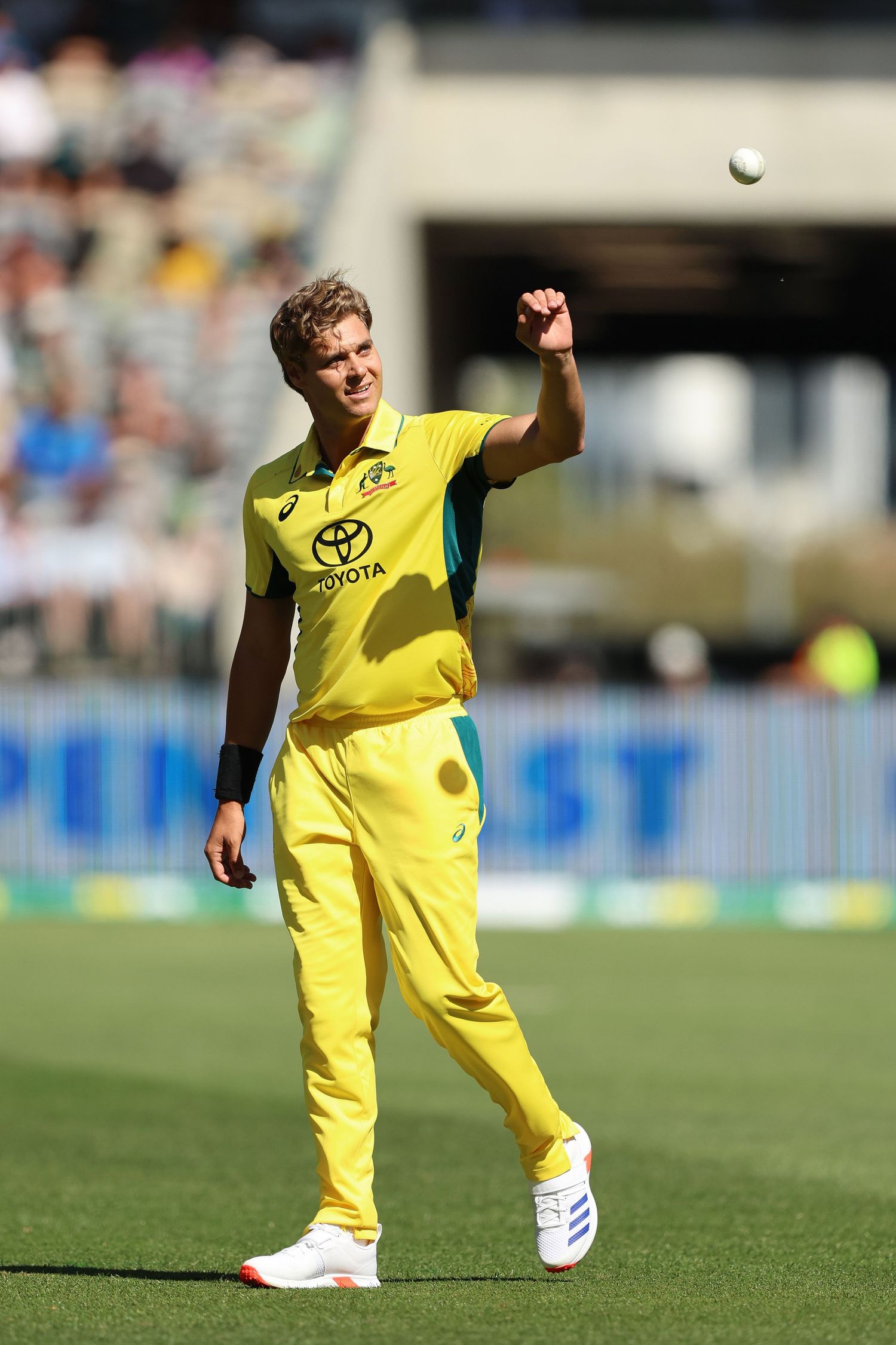 A cricket player in yellow uniform stretches on the field during a match under bright sunlight.