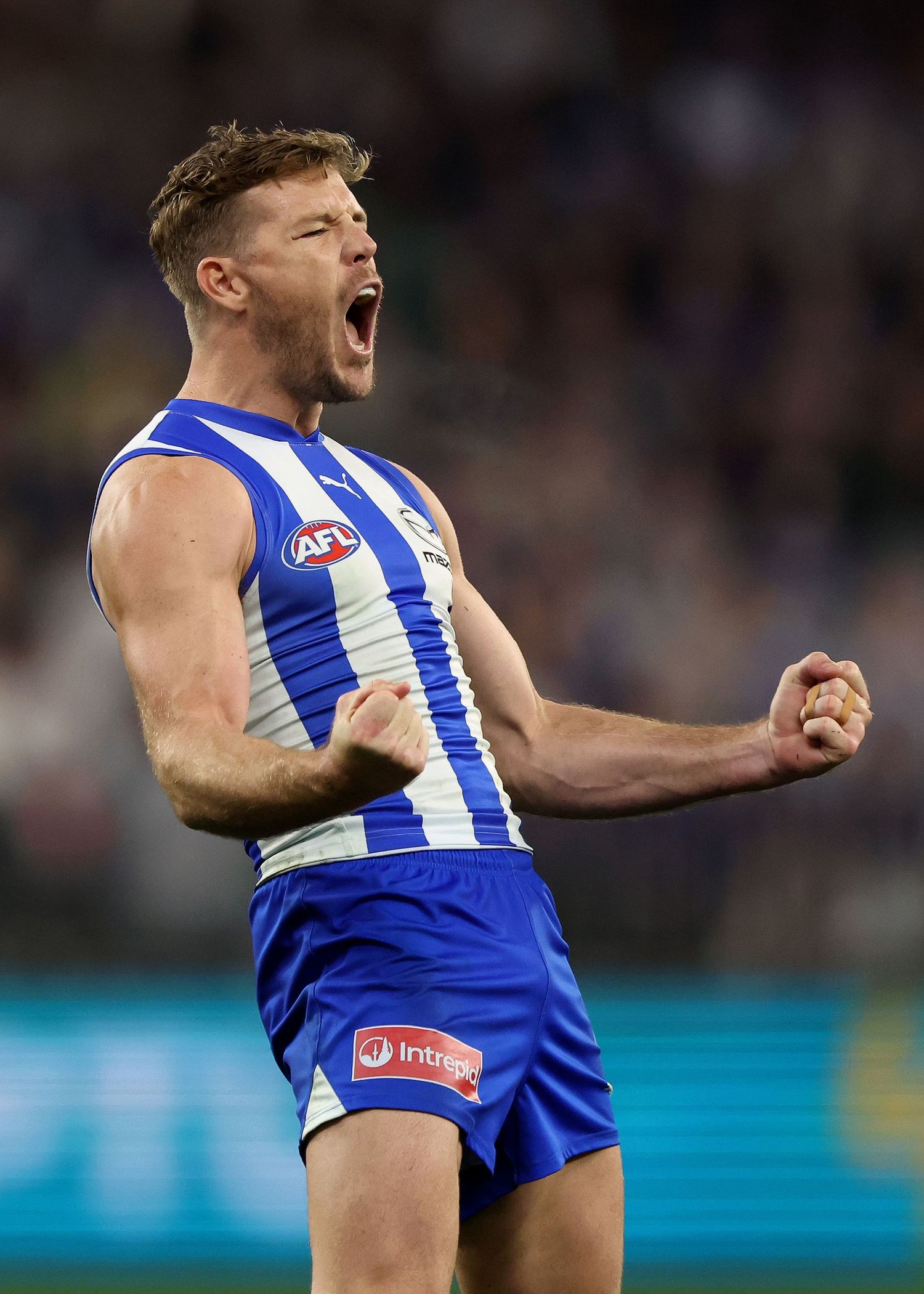 AFL player celebrates passionately in blue and white striped uniform after scoring during intense match.