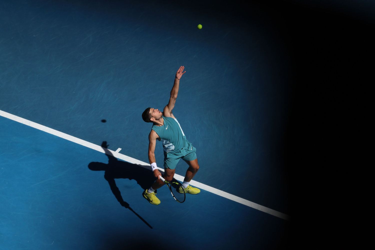 Tennis player serving ball on blue court during professional match.
