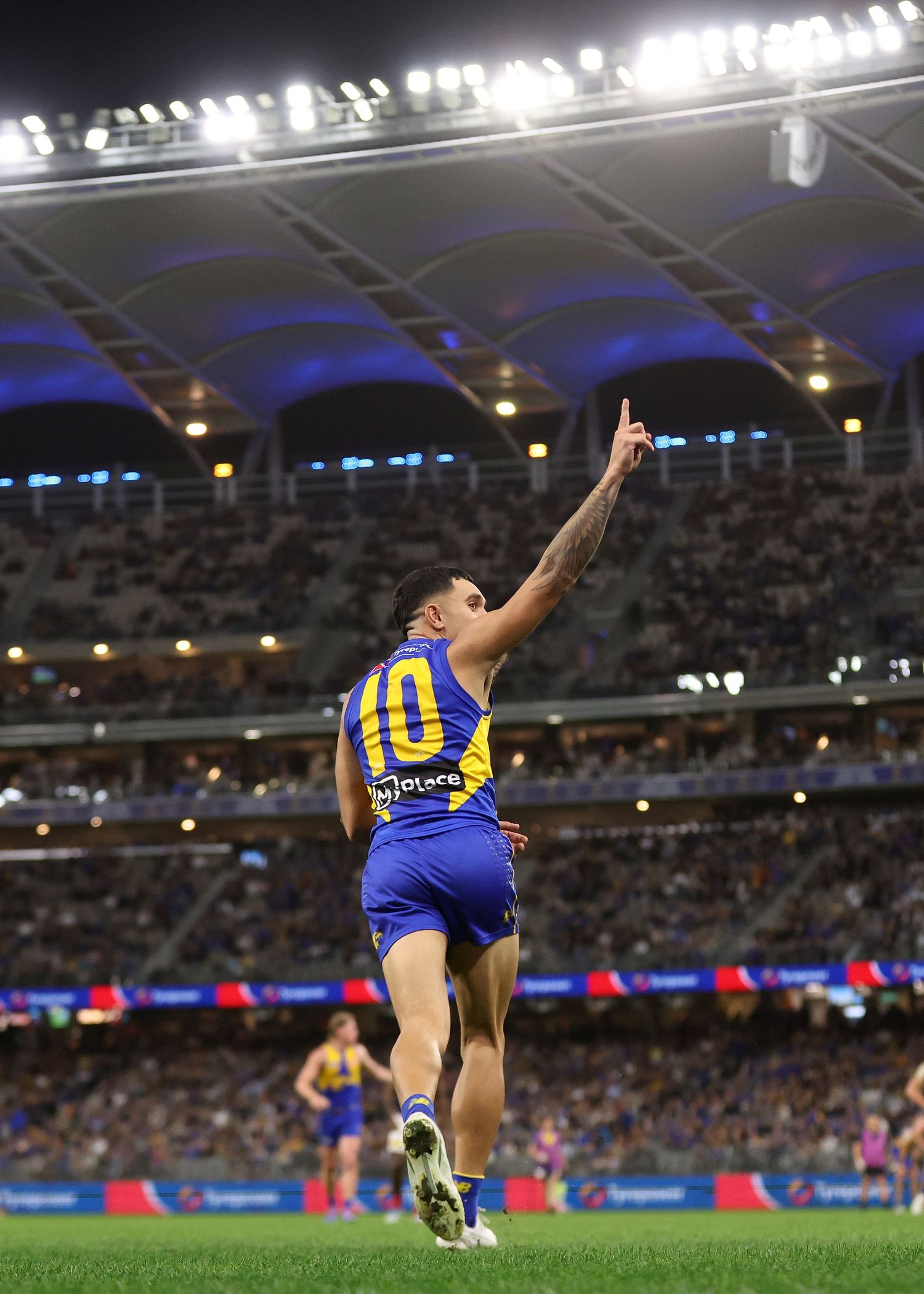 Player in blue and gold jumper reaches up to mark the ball under stadium lights.