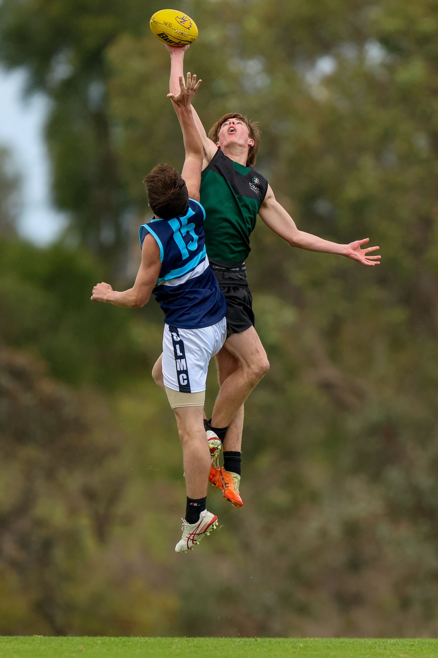 Two Australian Rules Football players leap high in the air to contest for possession of the yellow ball during a match.