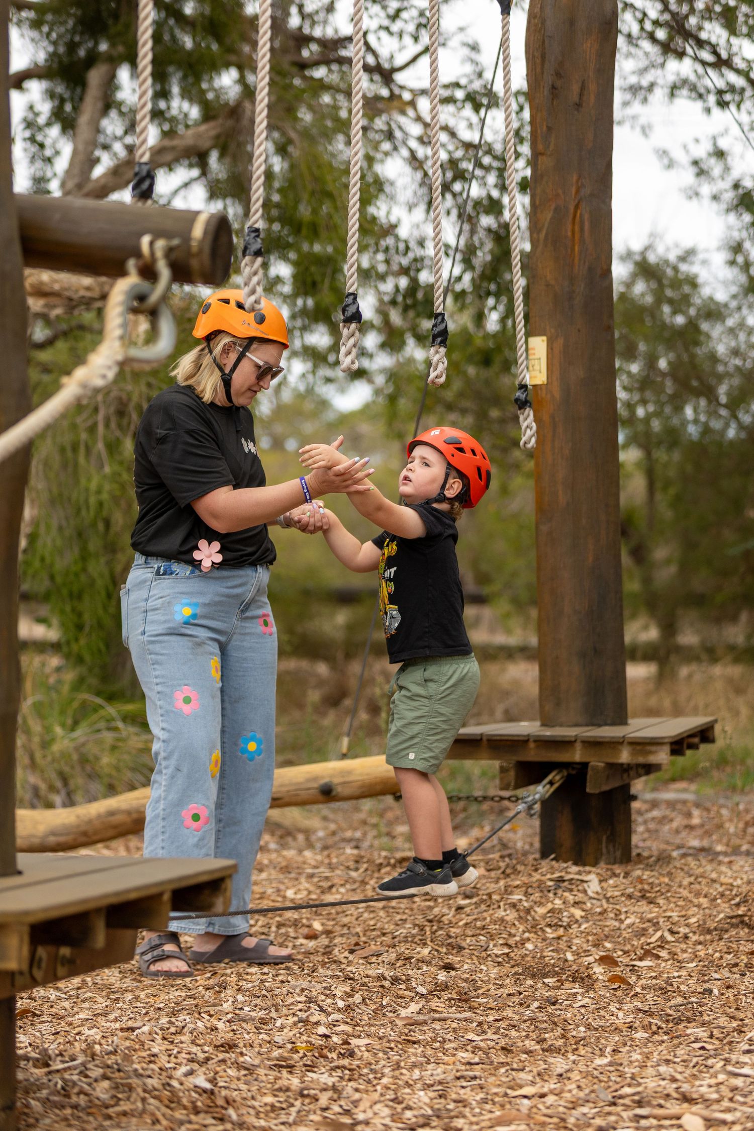 Two participants interacting on a wooden platform at a ropes course wearing safety helmets.