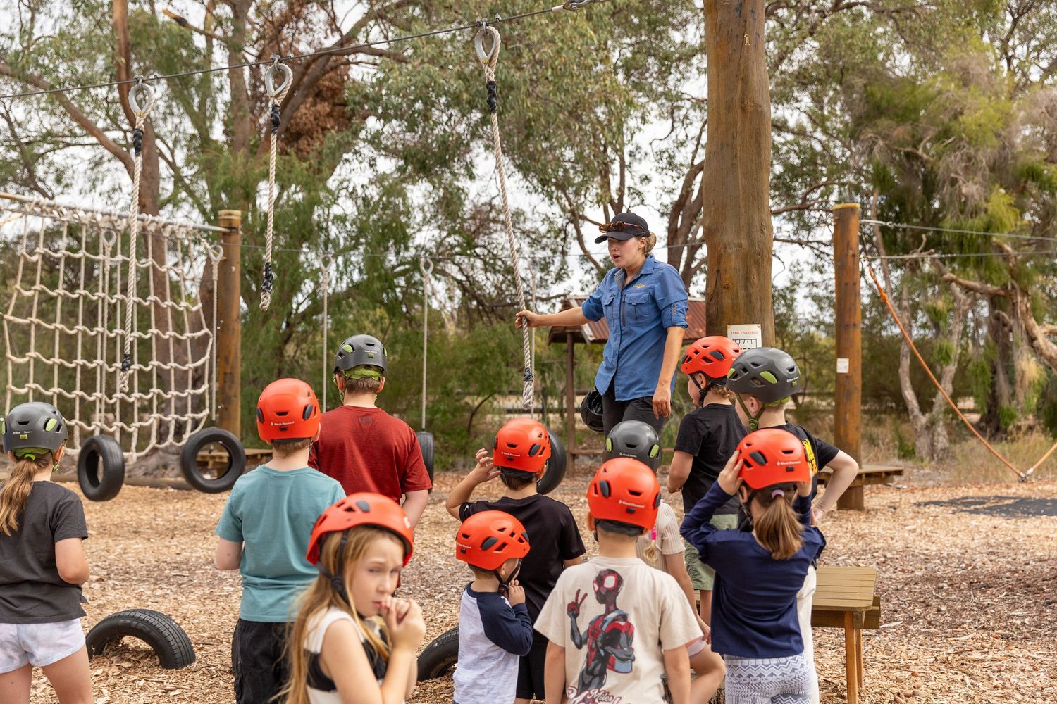 Group wearing orange helmets gathered outdoors for adventure activity instruction.
