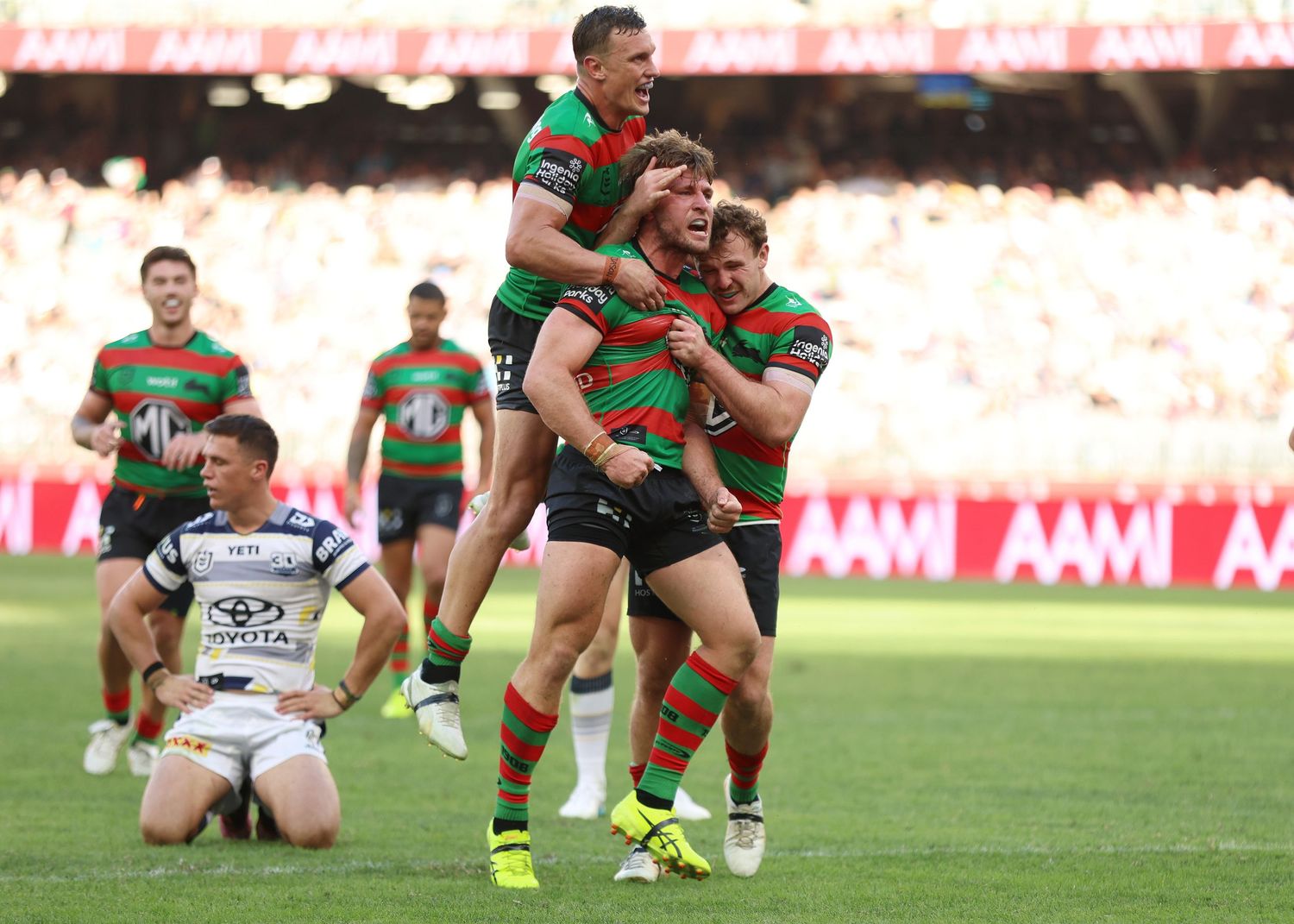 Rugby players in South Sydney Rabbitohs jerseys celebrate together after scoring a try.