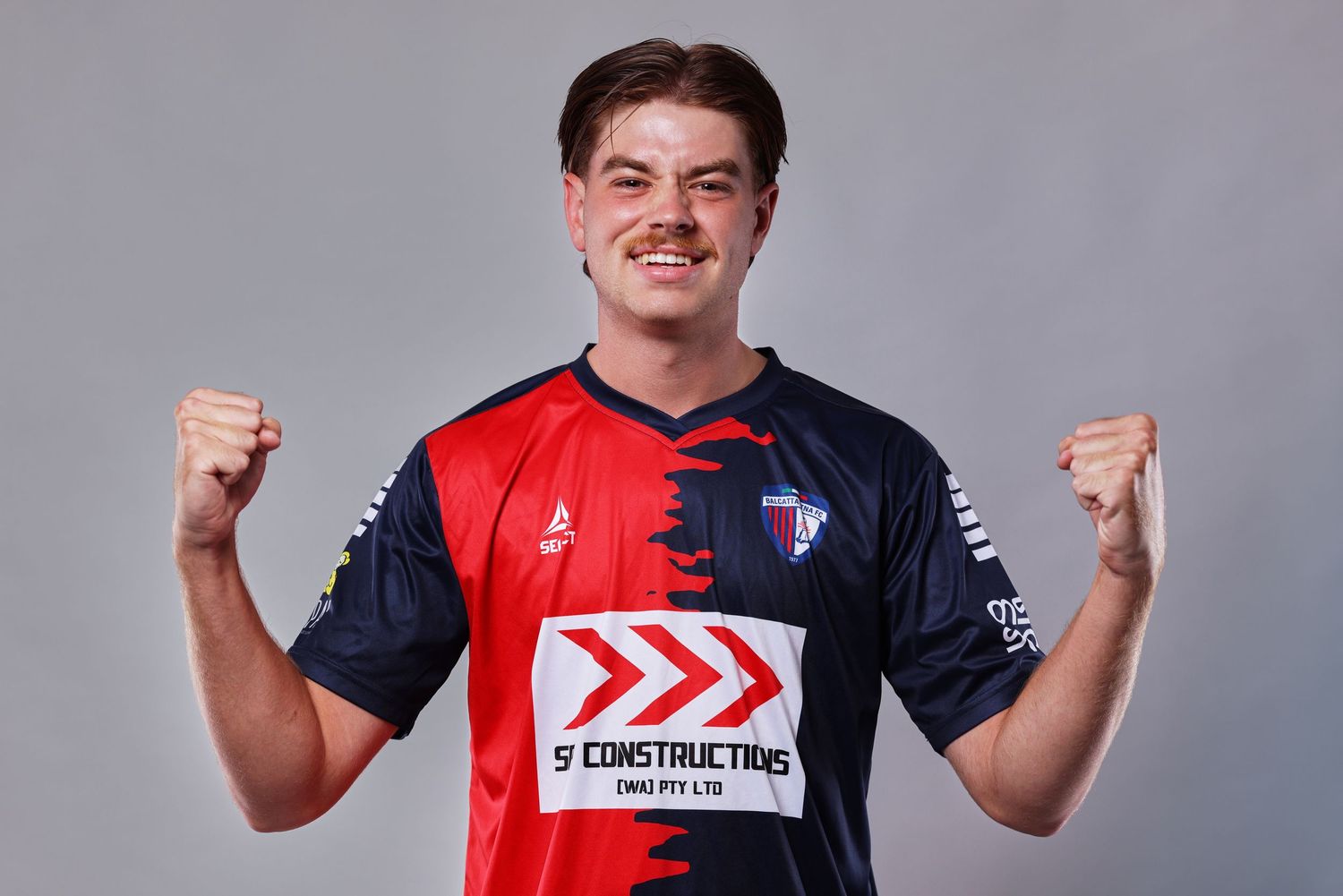 Professional athlete poses in red and navy blue sports uniform against gray background.