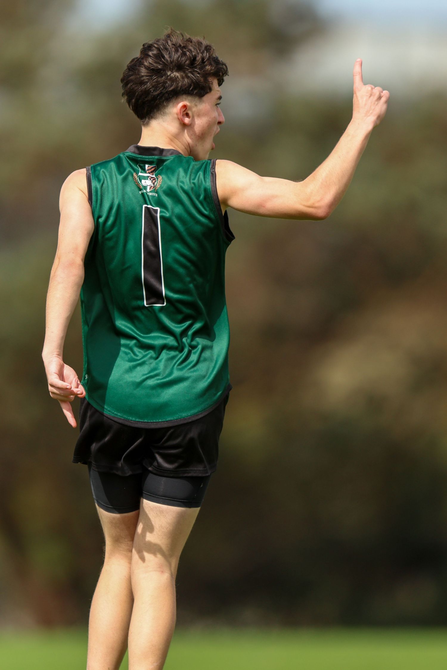 Sequential motion shots of an athlete wearing a green jersey and black shorts demonstrating a jumping technique outdoors.