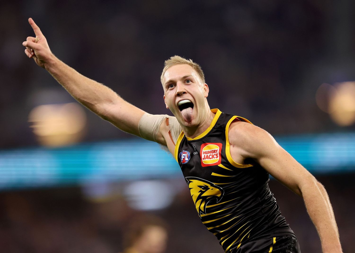 AFL football player in yellow and black Richmond Tigers uniform celebrates with his finger pointed skyward during a game.