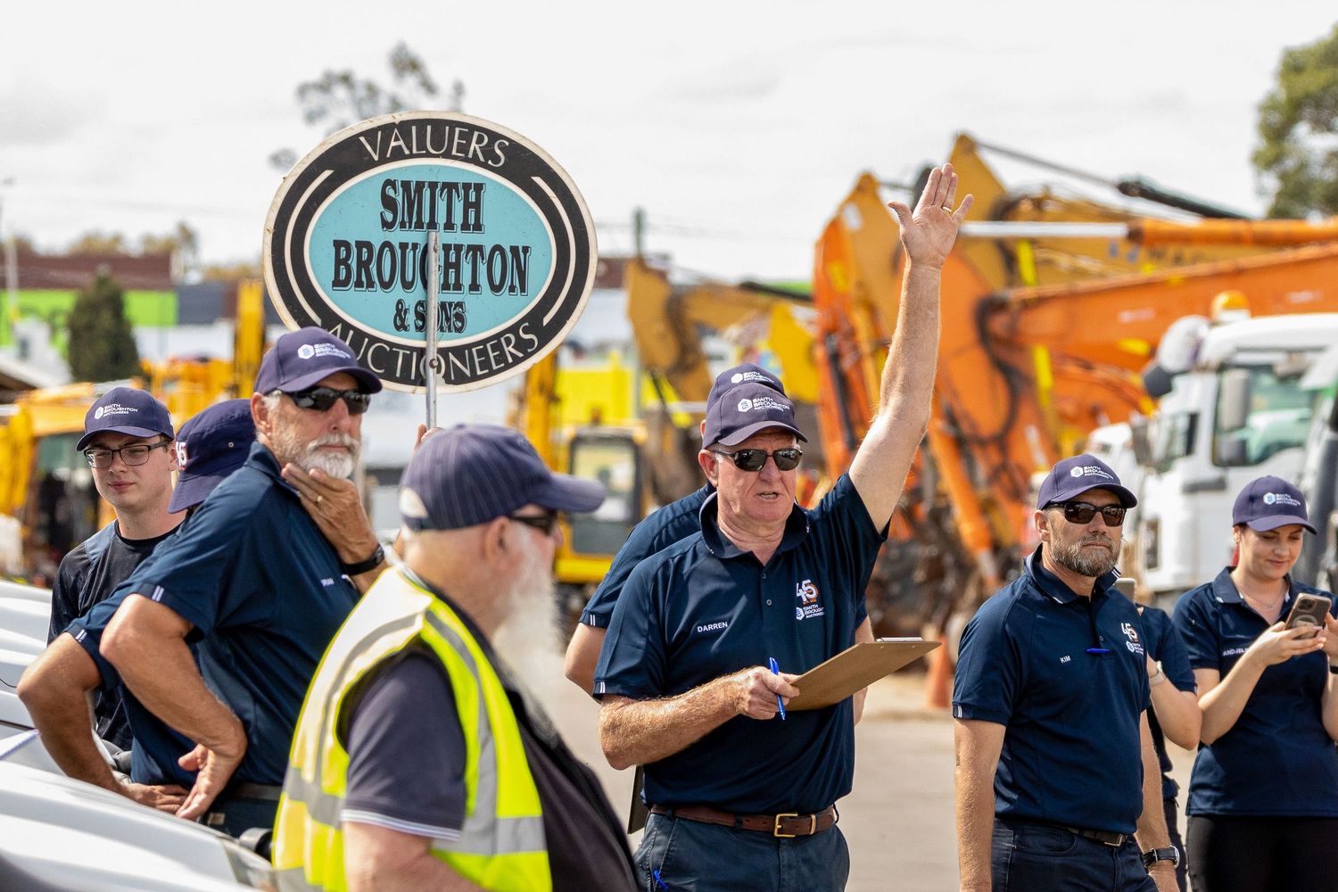 Construction crew members gather for a safety briefing near heavy equipment at an outdoor work site.