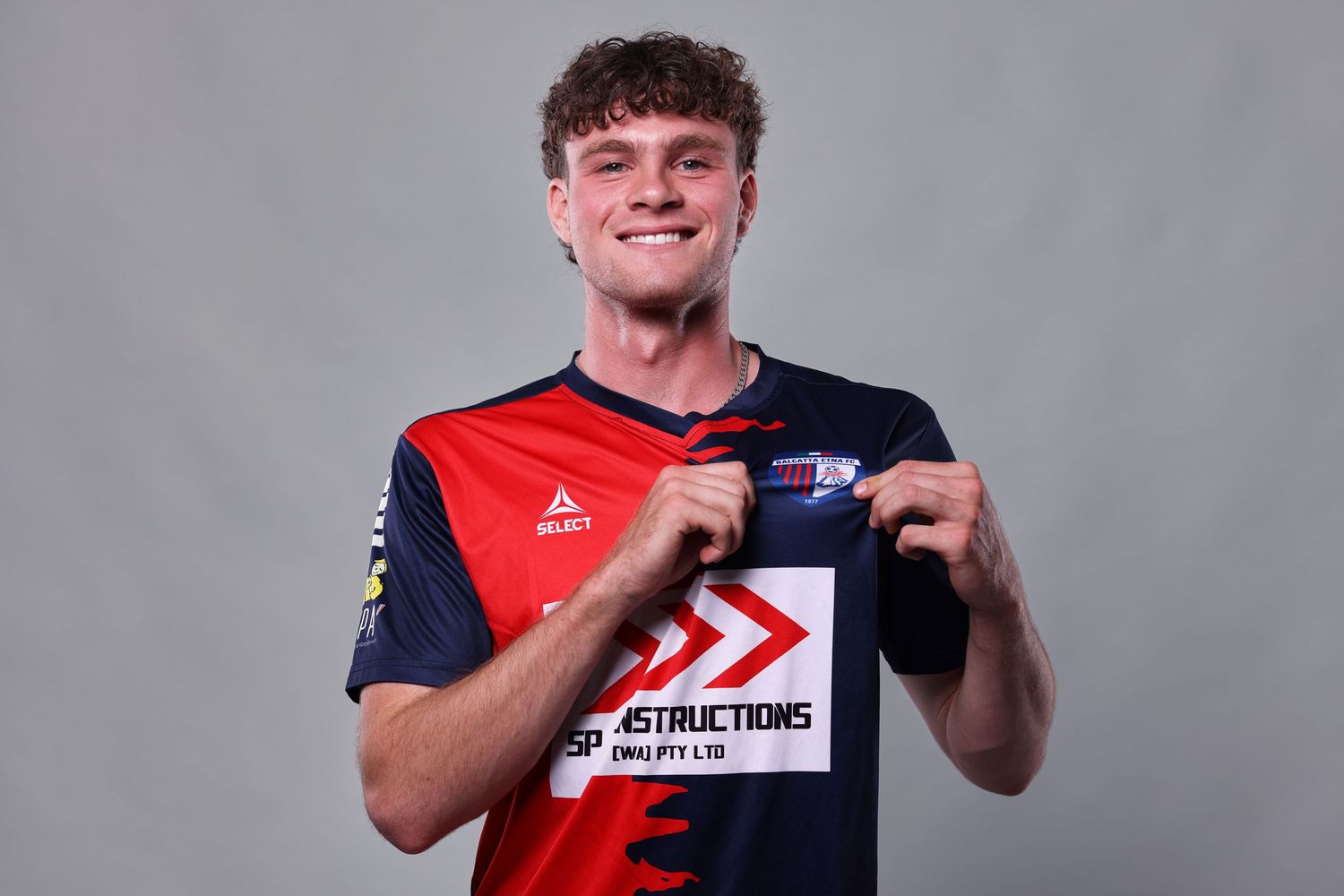 Professional soccer player in red and navy uniform poses with arms crossed during team photo session.
