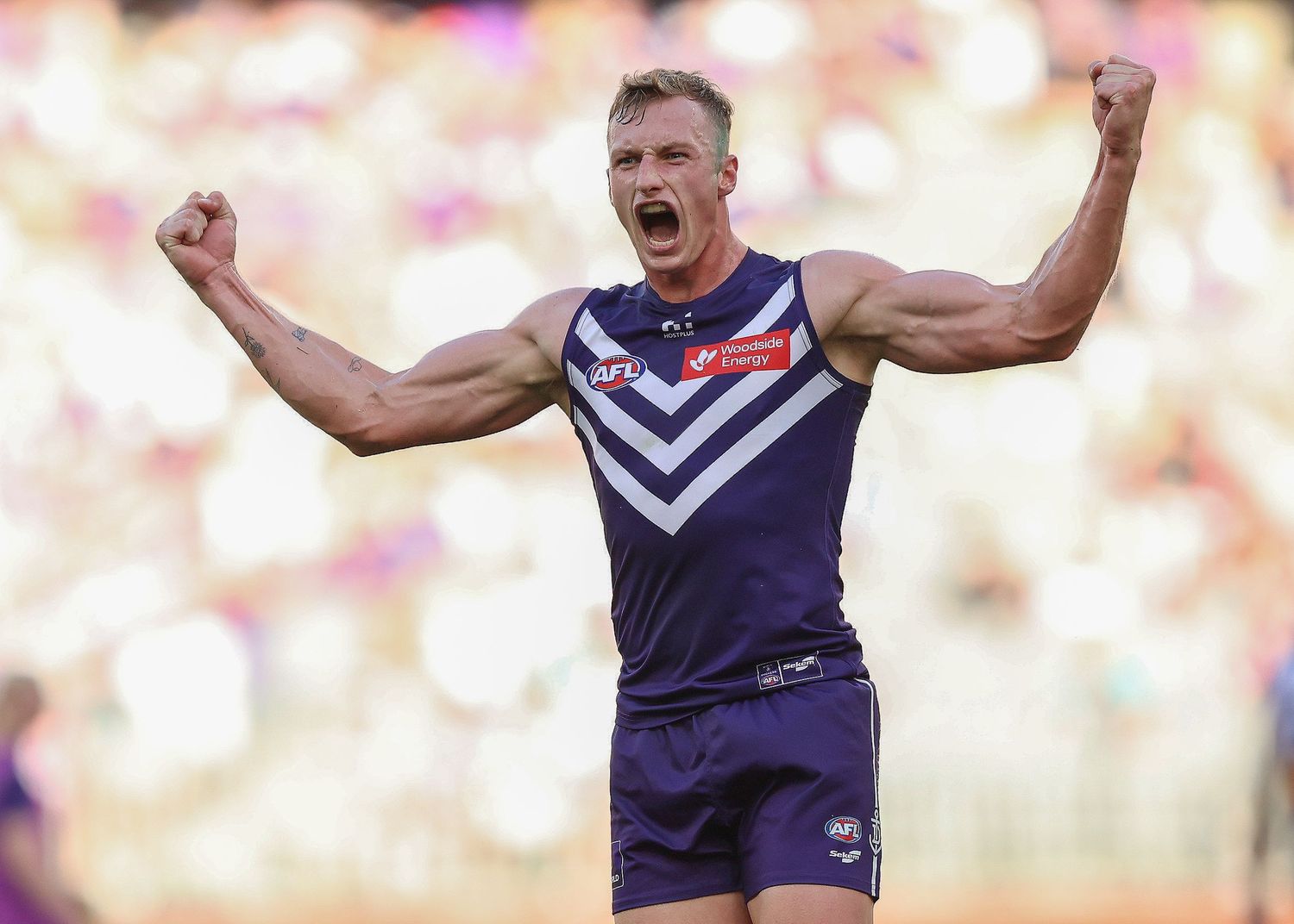 Player in navy blue uniform celebrates with arms raised during AFL match.