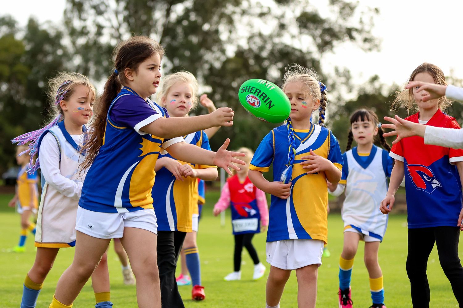 Children in sports uniforms playing with a green balloon on a grassy field during outdoor activities.