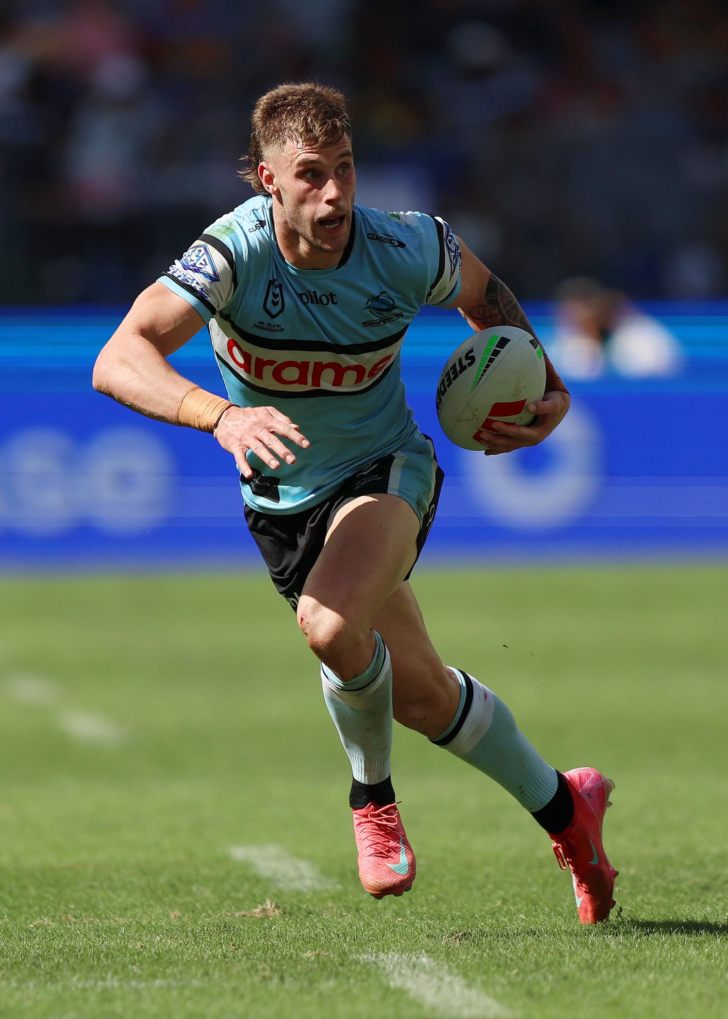 Rugby player carries ball while running in light blue Sharks uniform during match.