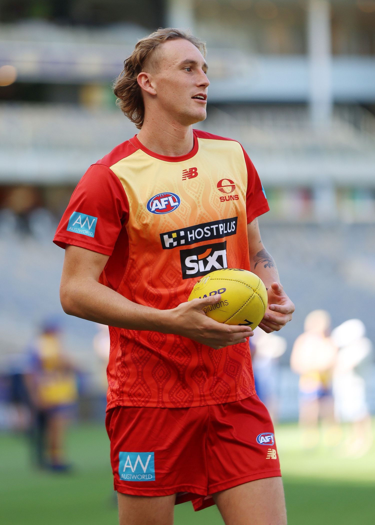 Player in red and yellow AFL training uniform holds football during practice session.