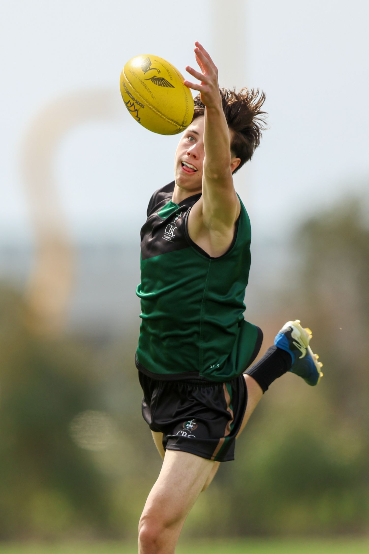 Australian Rules Football player leaps high in the air wearing a green jersey to catch the ball during a match.
