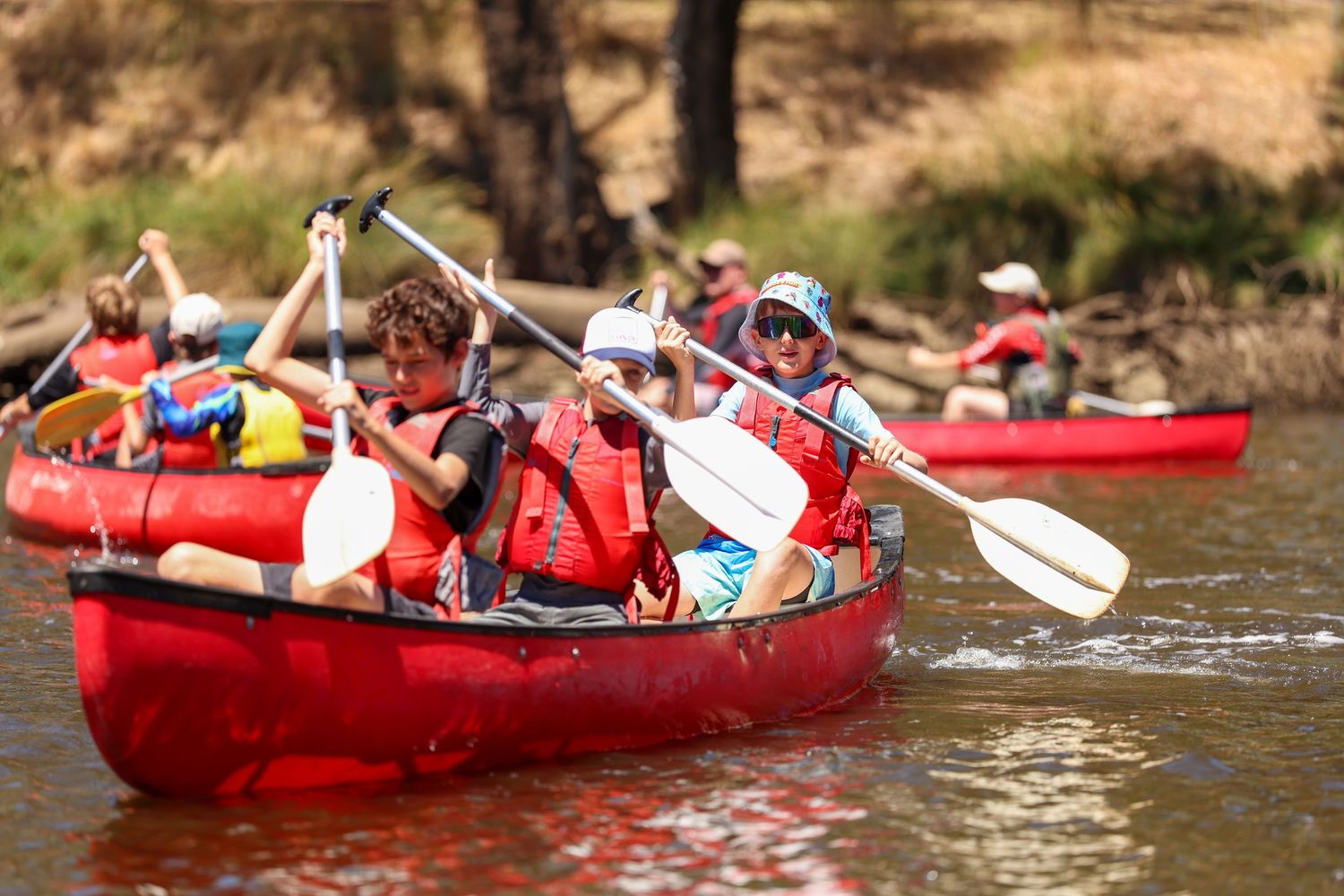 Red rafts filled with adventurous rafters navigate through scenic river waters during a summer excursion.