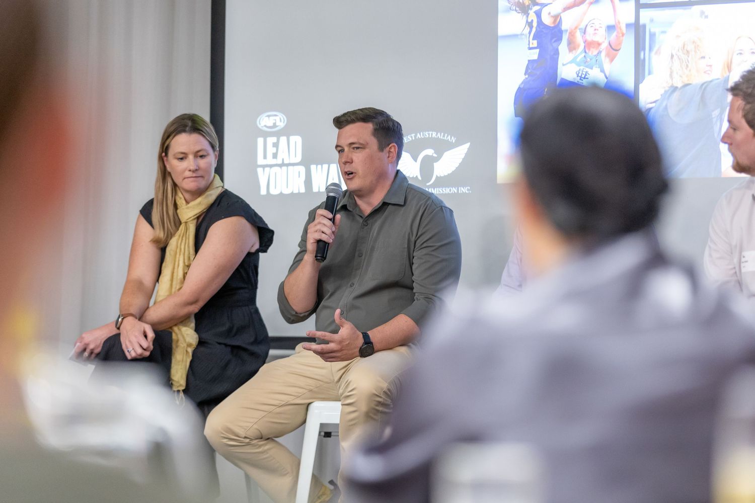 Two panelists engaged in conversation while sitting on stage at a professional speaking event.