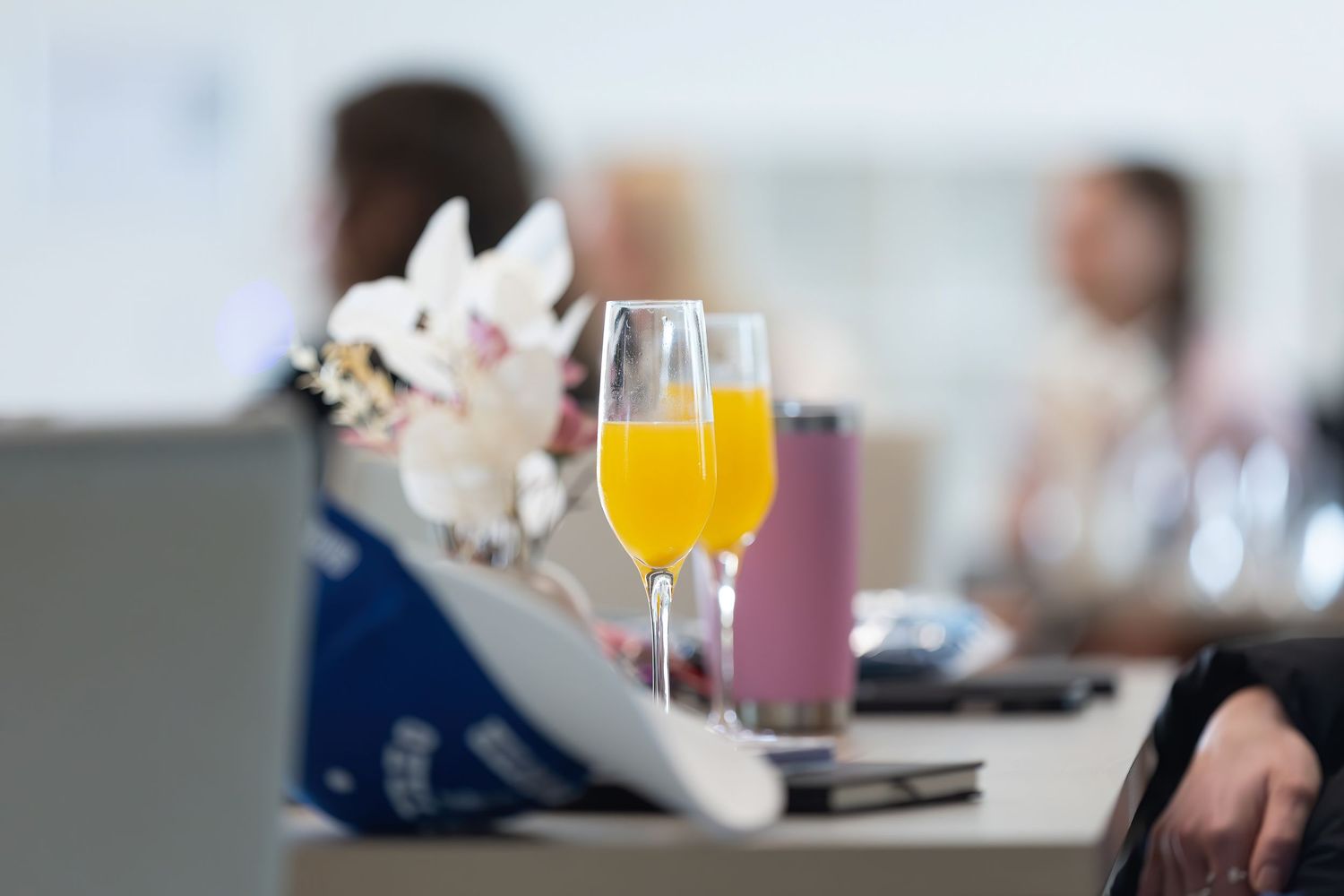 A mimosa cocktail in a champagne flute sits on a table with delicate white flowers in soft focus.
