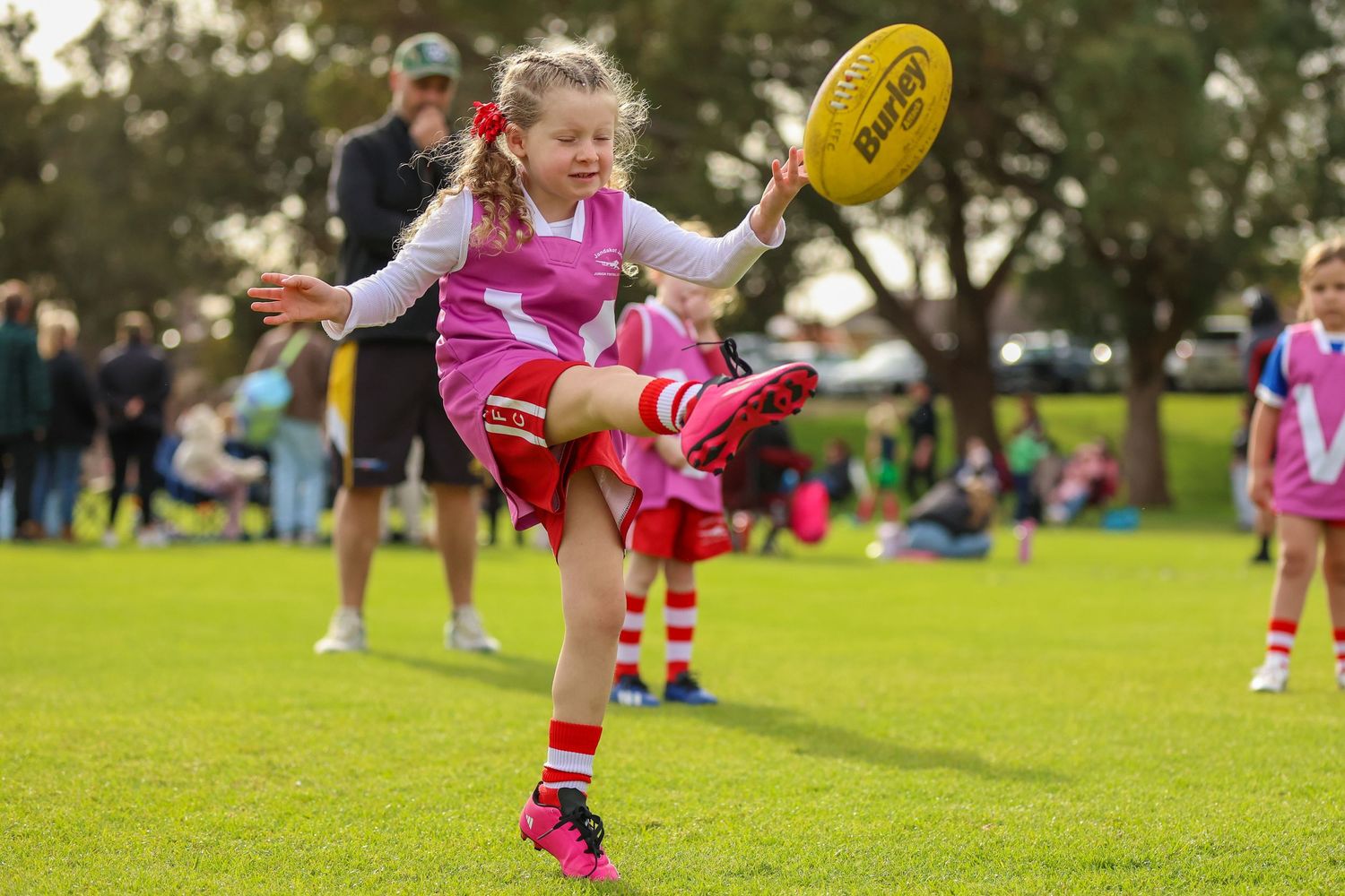 An Australian rules football player in bright pink shorts jumps to catch a yellow football during an outdoor match.