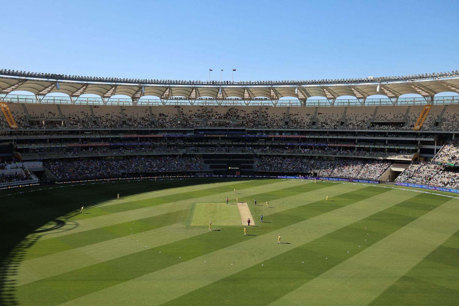 Modern cricket stadium with distinctive curved roof architecture and well-maintained green pitch.