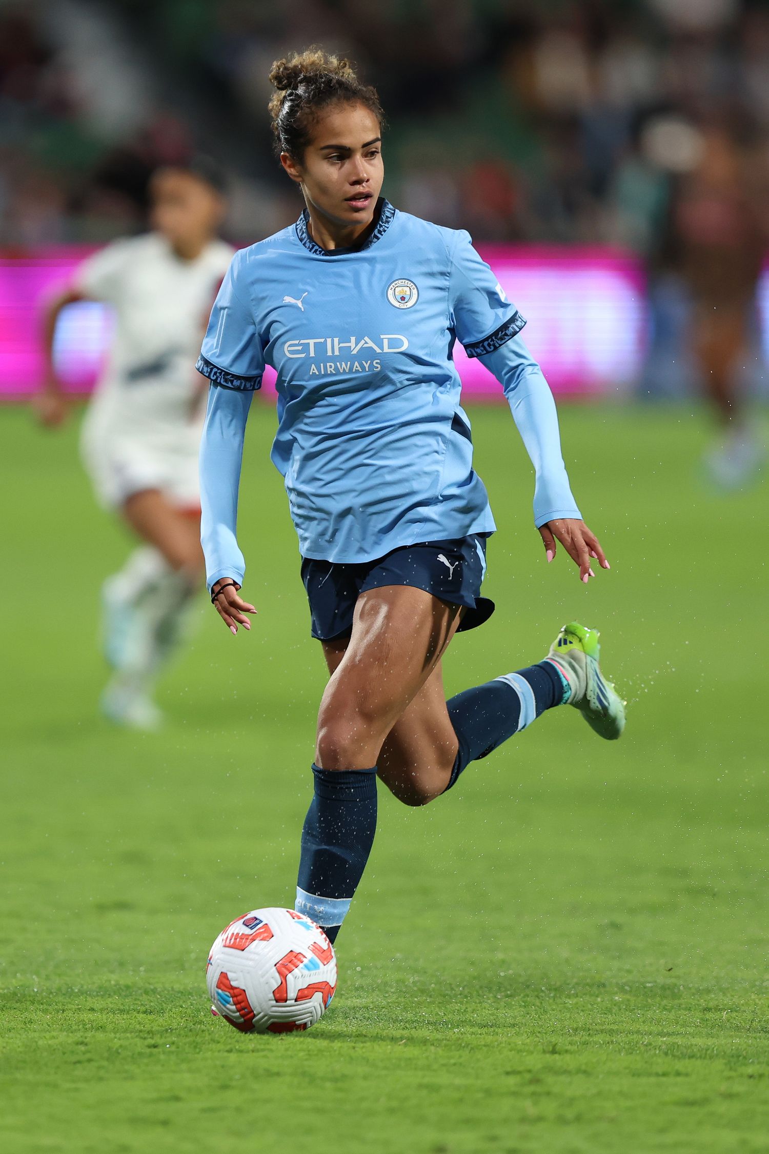 Soccer player in light blue Manchester City uniform dribbles ball during match.