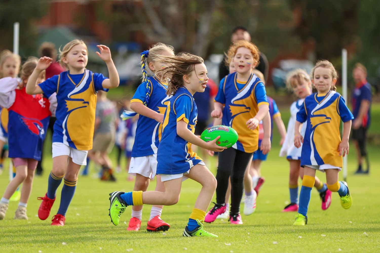 Children's soccer team in blue and yellow uniforms practicing and running on a green grass field during training session.