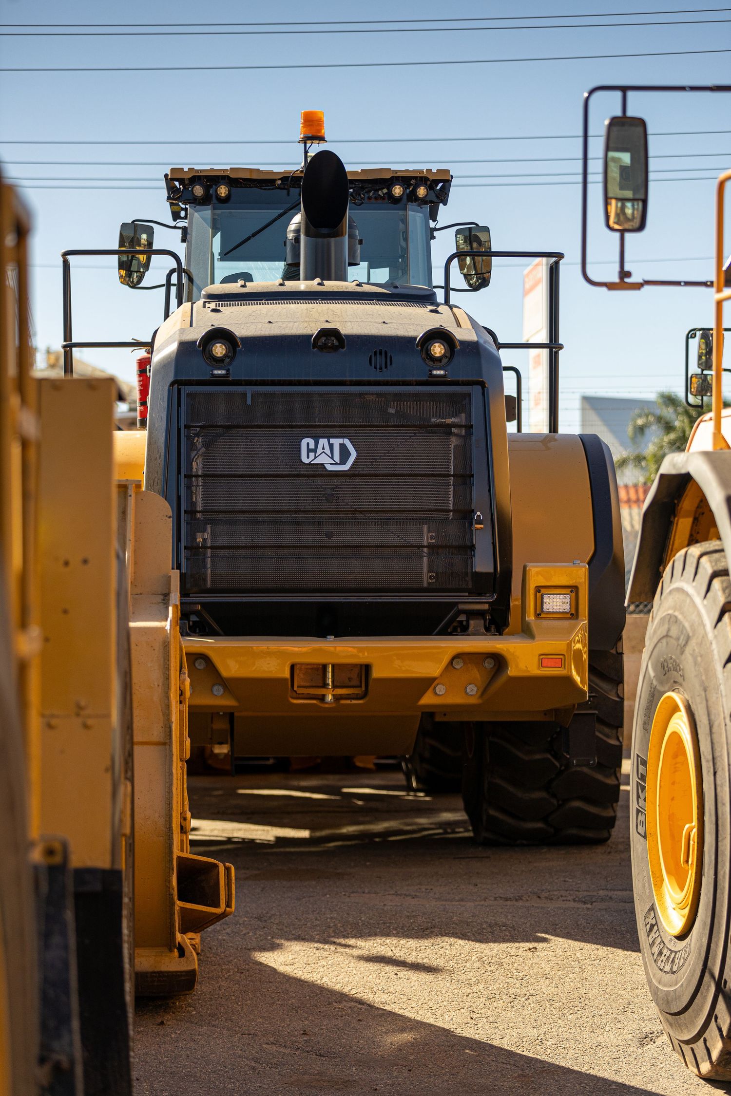 Close-up view of heavy equipment machinery with CAT branding at a construction site with power lines visible above.