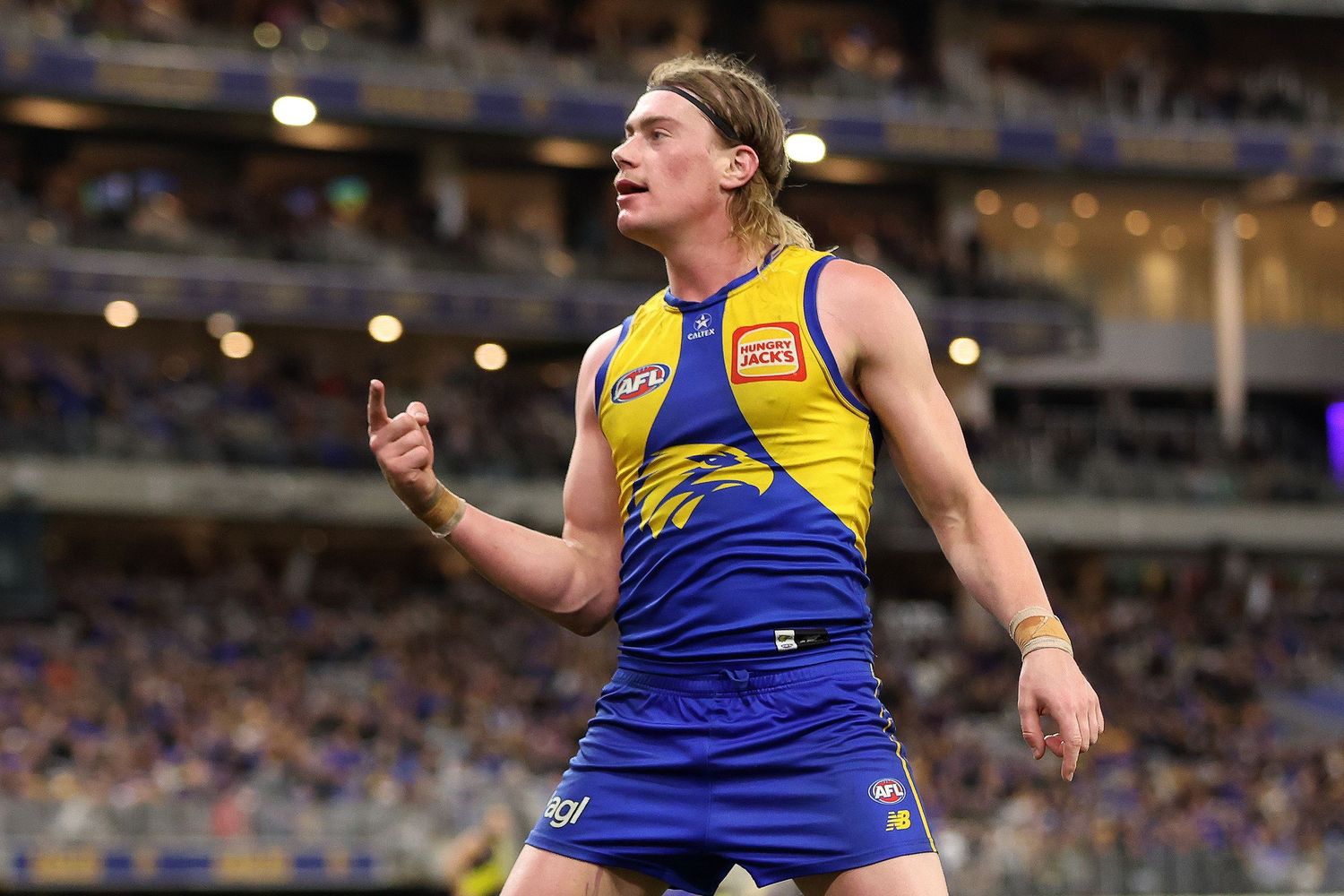 AFL player in blue and gold uniform celebrates with raised arms after scoring during match at stadium.