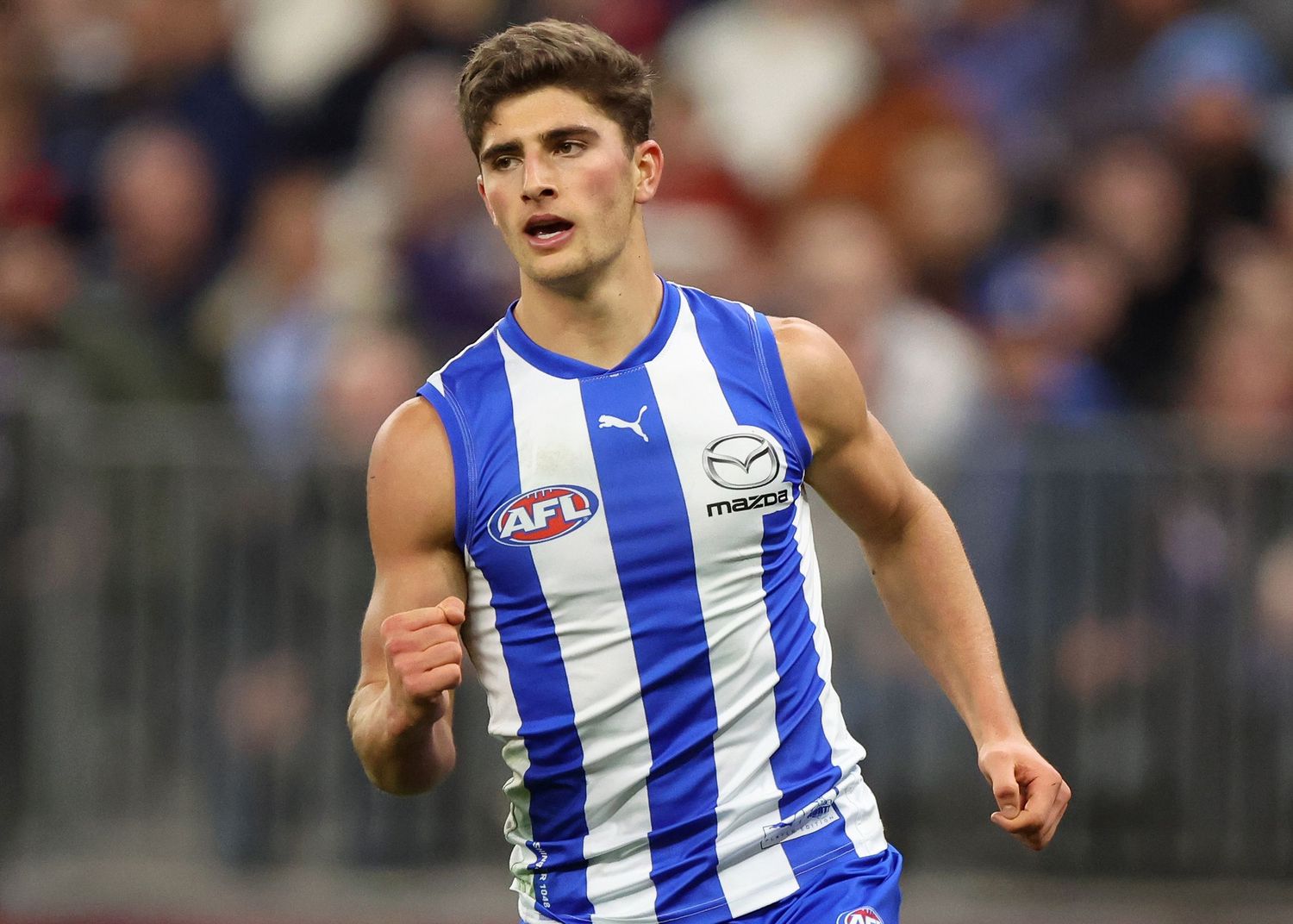 AFL player in blue and white striped North Melbourne Kangaroos uniform running during a game.