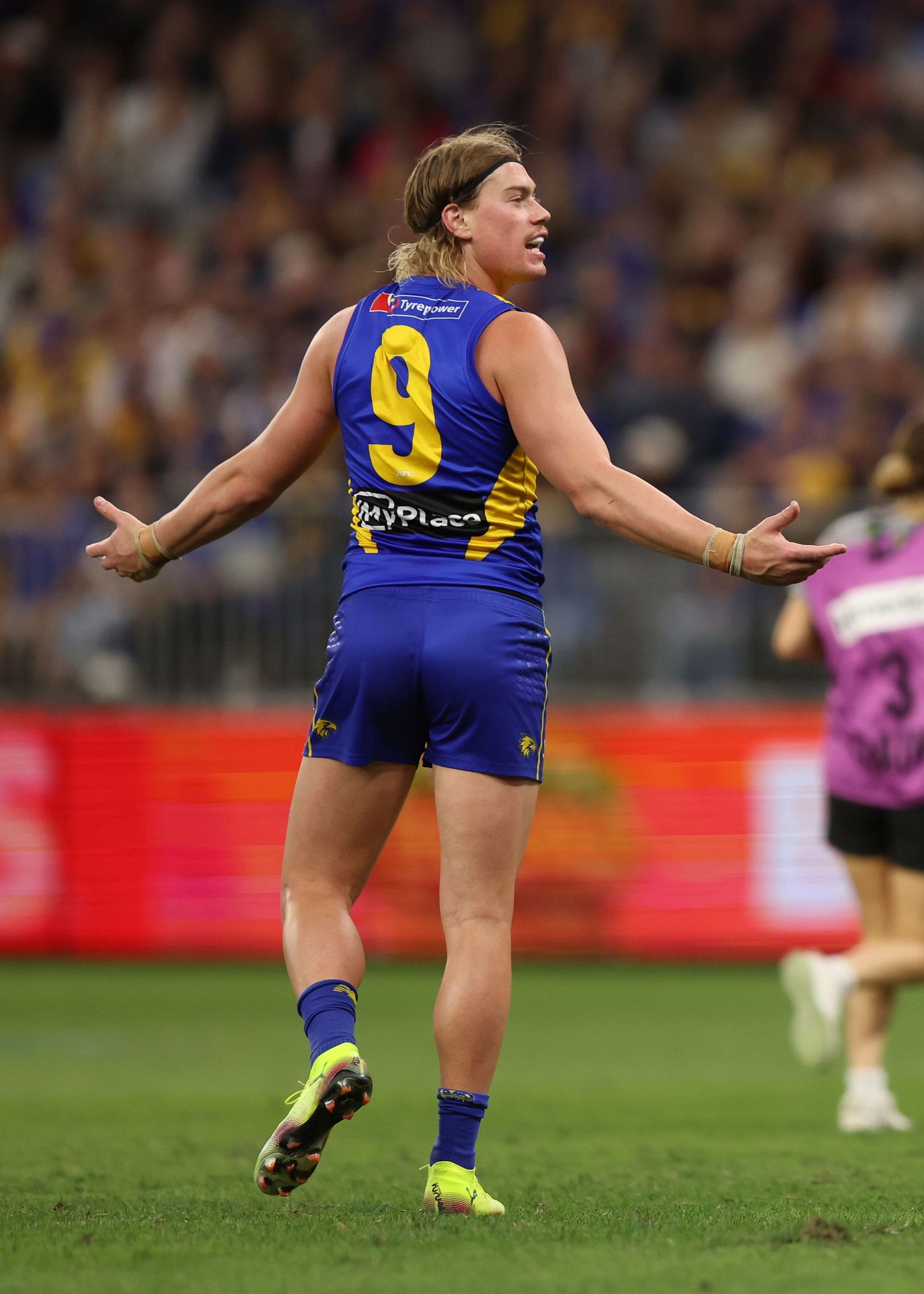 AFL player in blue and gold uniform gestures with arms outstretched during game.