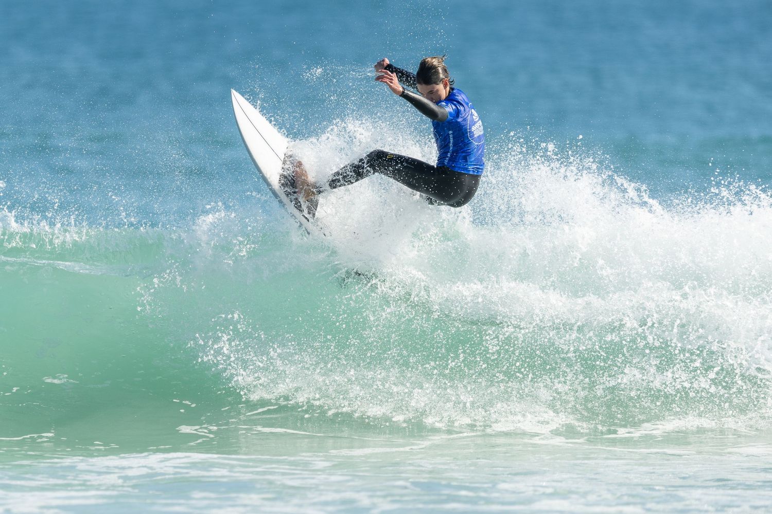 A surfer carves through a turquoise wave creating dramatic splashes and spray on a sunny day.