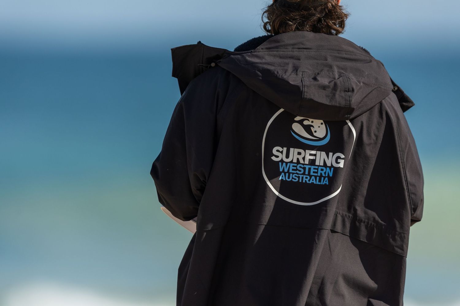 A collection of black surfer hoodies with various surfing-related logos and patches displayed against a blue background.