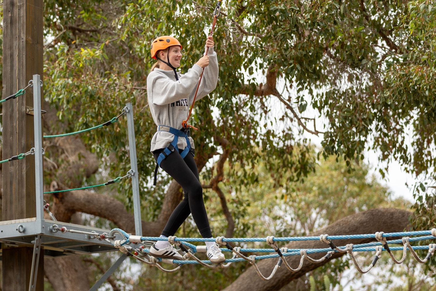 Participant in orange helmet and safety gear navigating elevated rope course platform.
