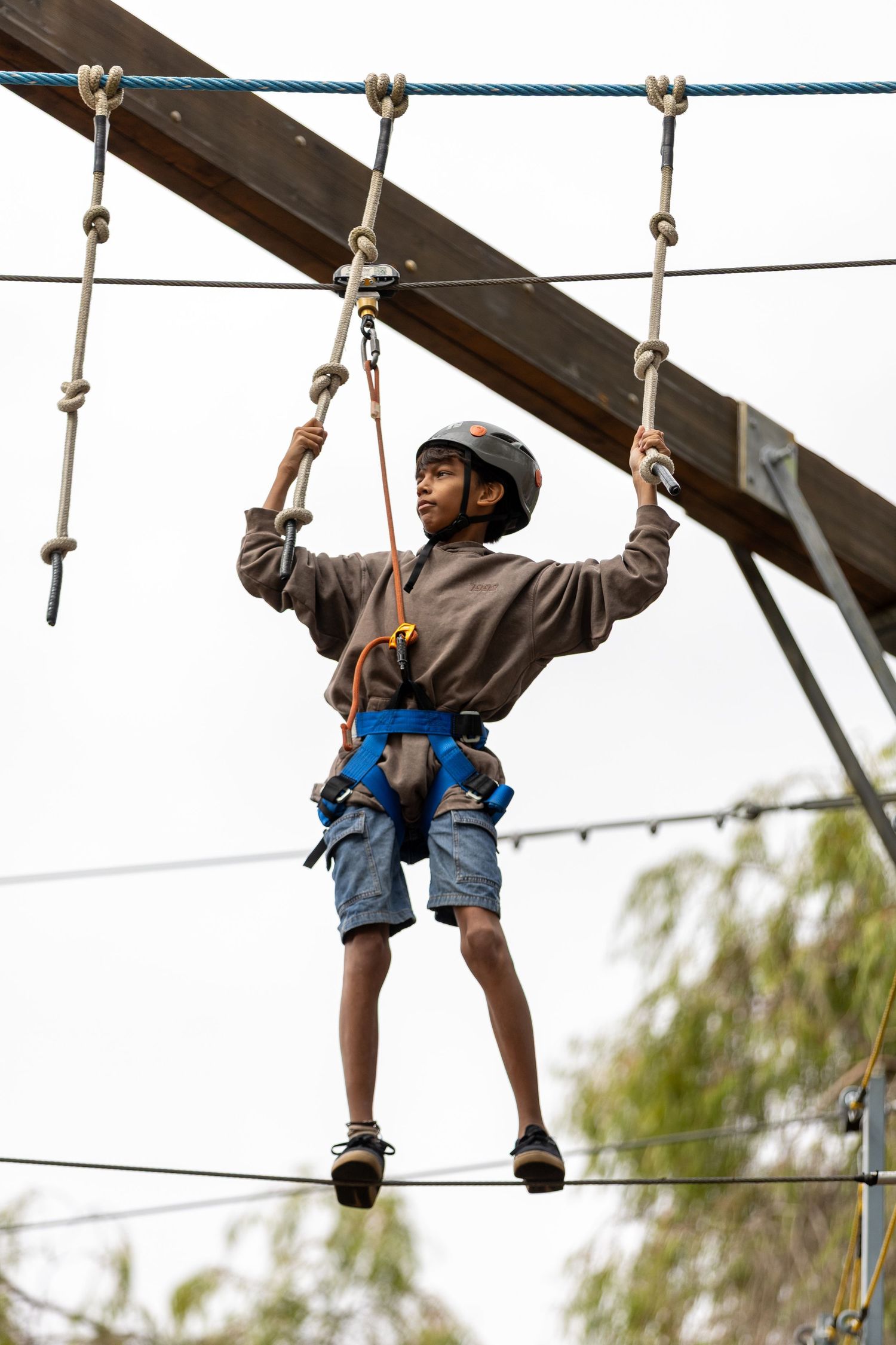 Person wearing safety harness and helmet traverses rope obstacle course elements.