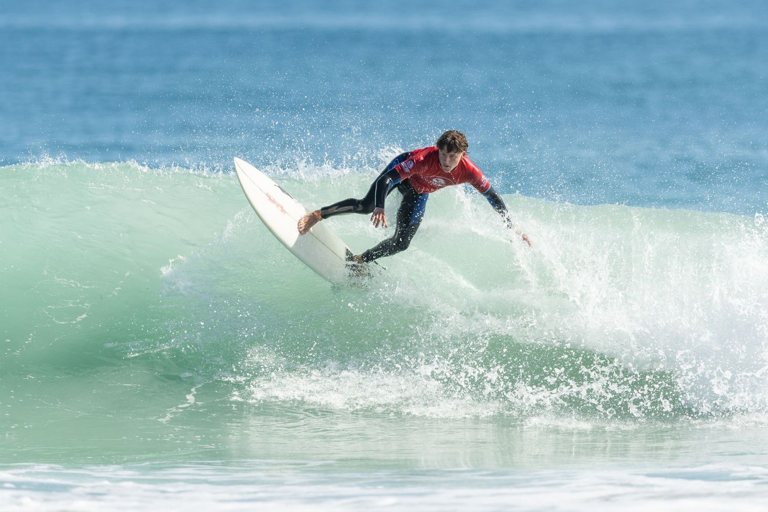 Professional surfer performs aerial maneuver off turquoise wave at surfing competition.