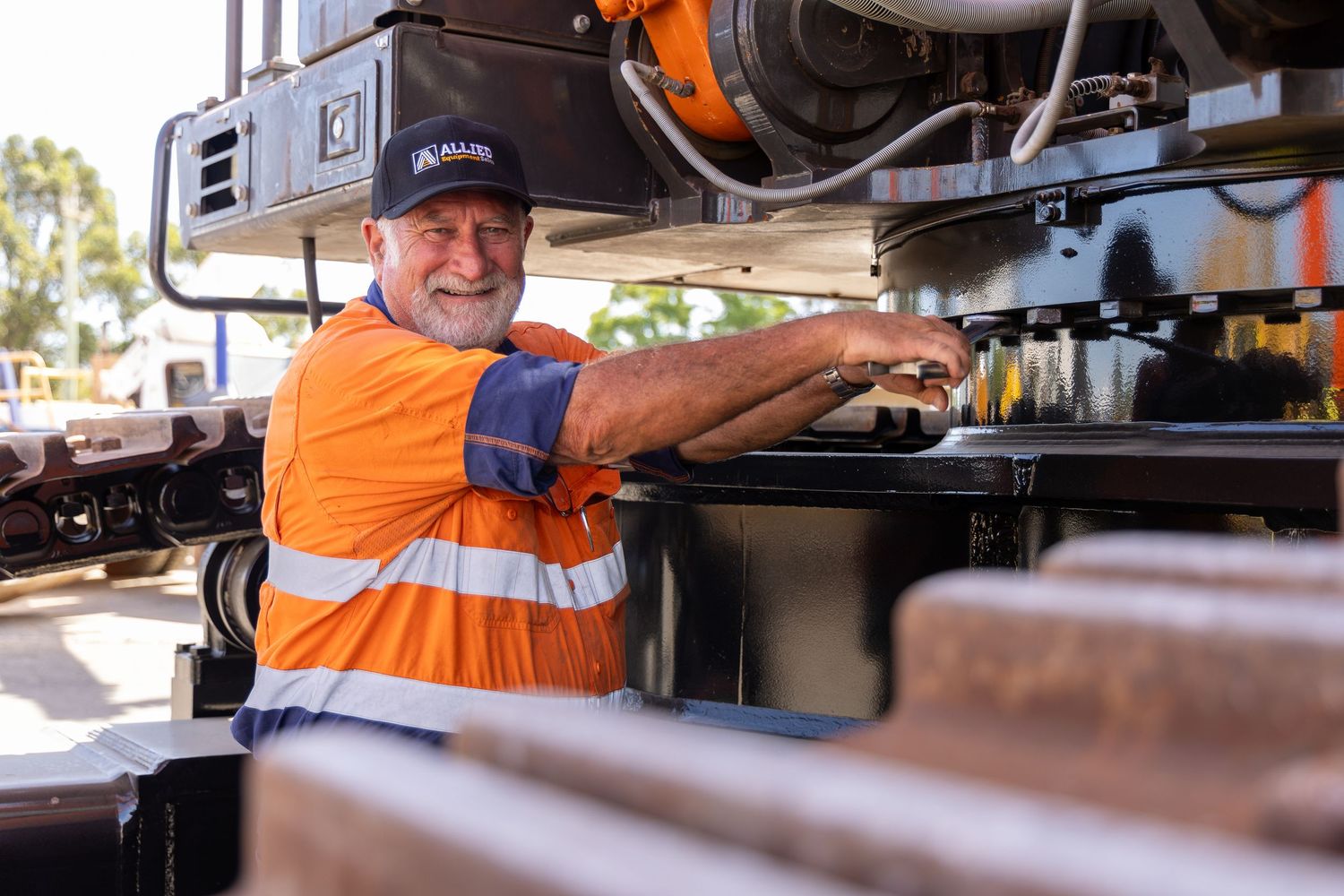 Worker in high-visibility orange vest operates machinery on a construction or maintenance site during daytime.