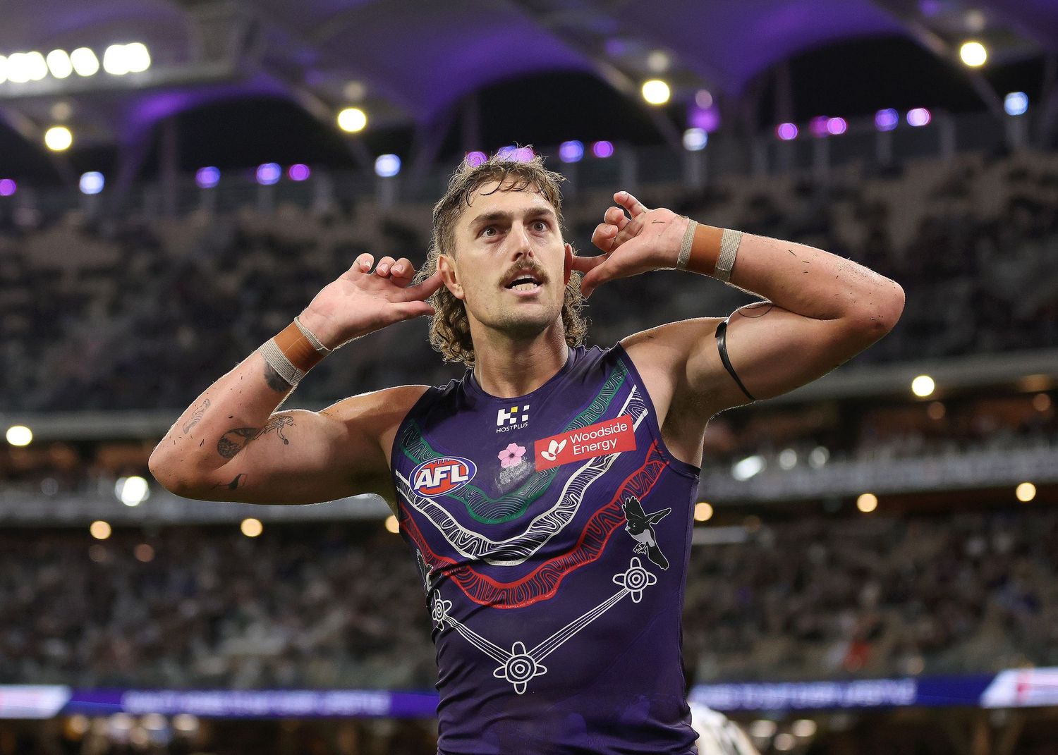 Track and field athlete gestures emotionally during competition at a stadium with purple lighting and blurred background.