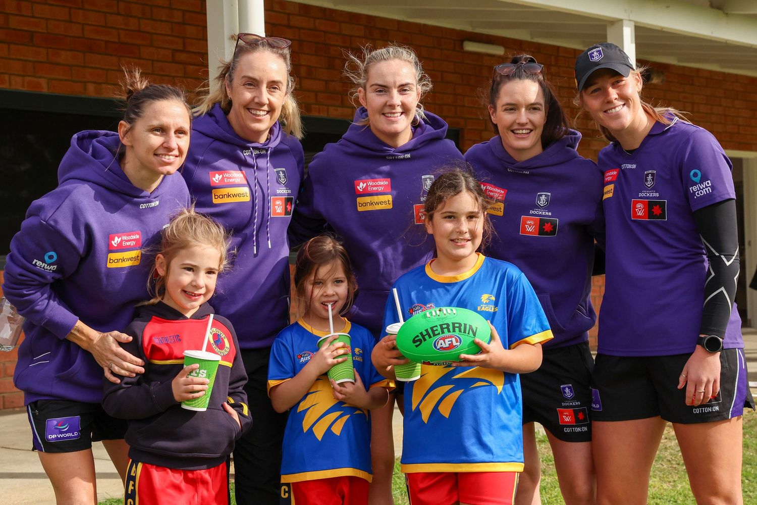 Youth sports team players in purple uniforms pose with drinks and snacks during a break.