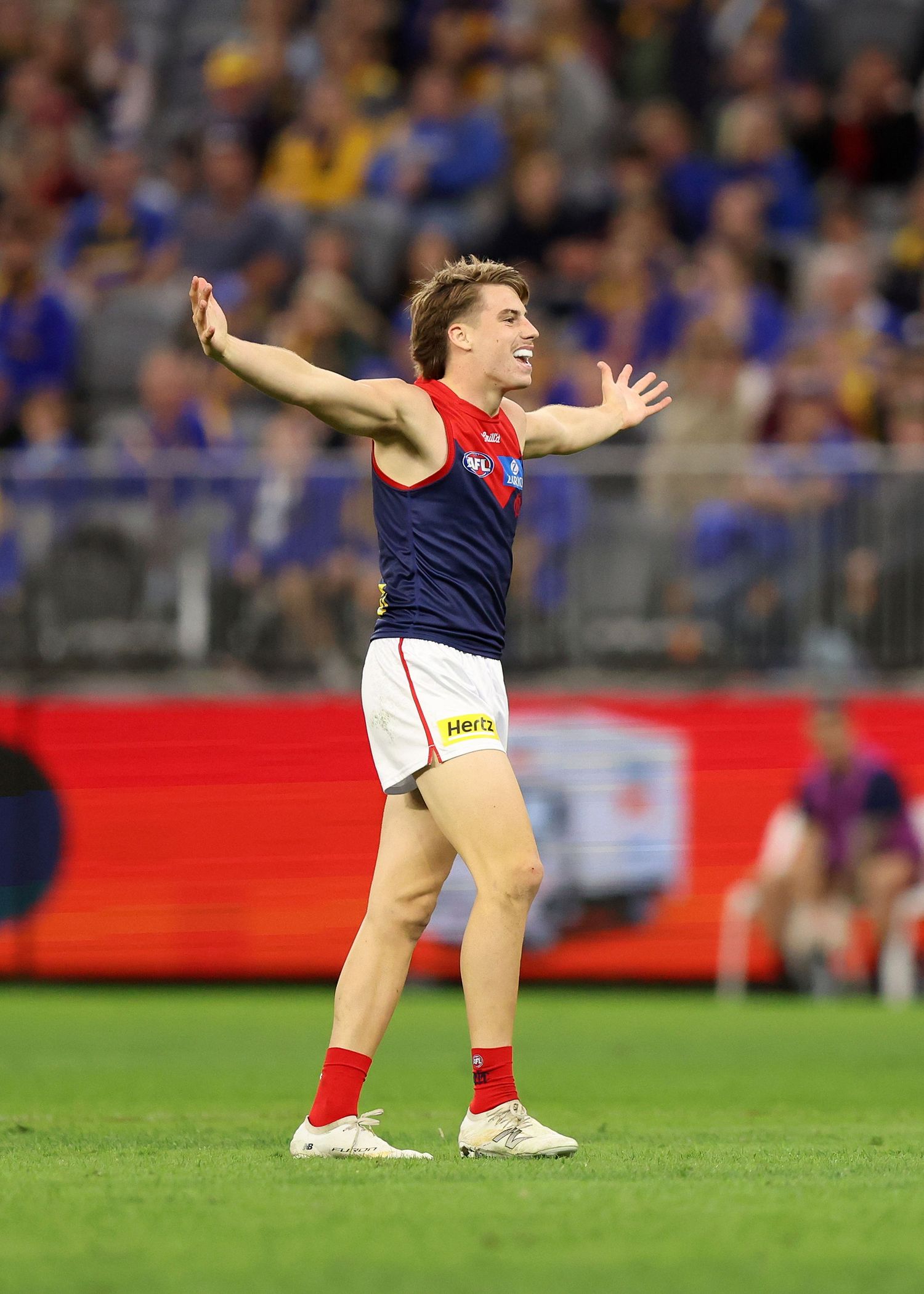 Player in red and blue uniform celebrates with arms outstretched on the field.