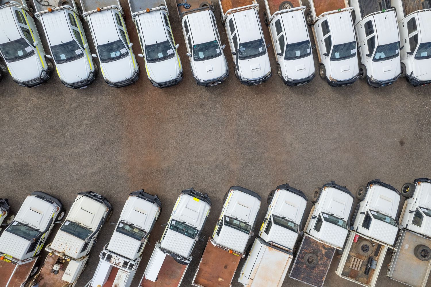 Aerial view of identical white vehicles parked in parallel rows at a dealership lot.