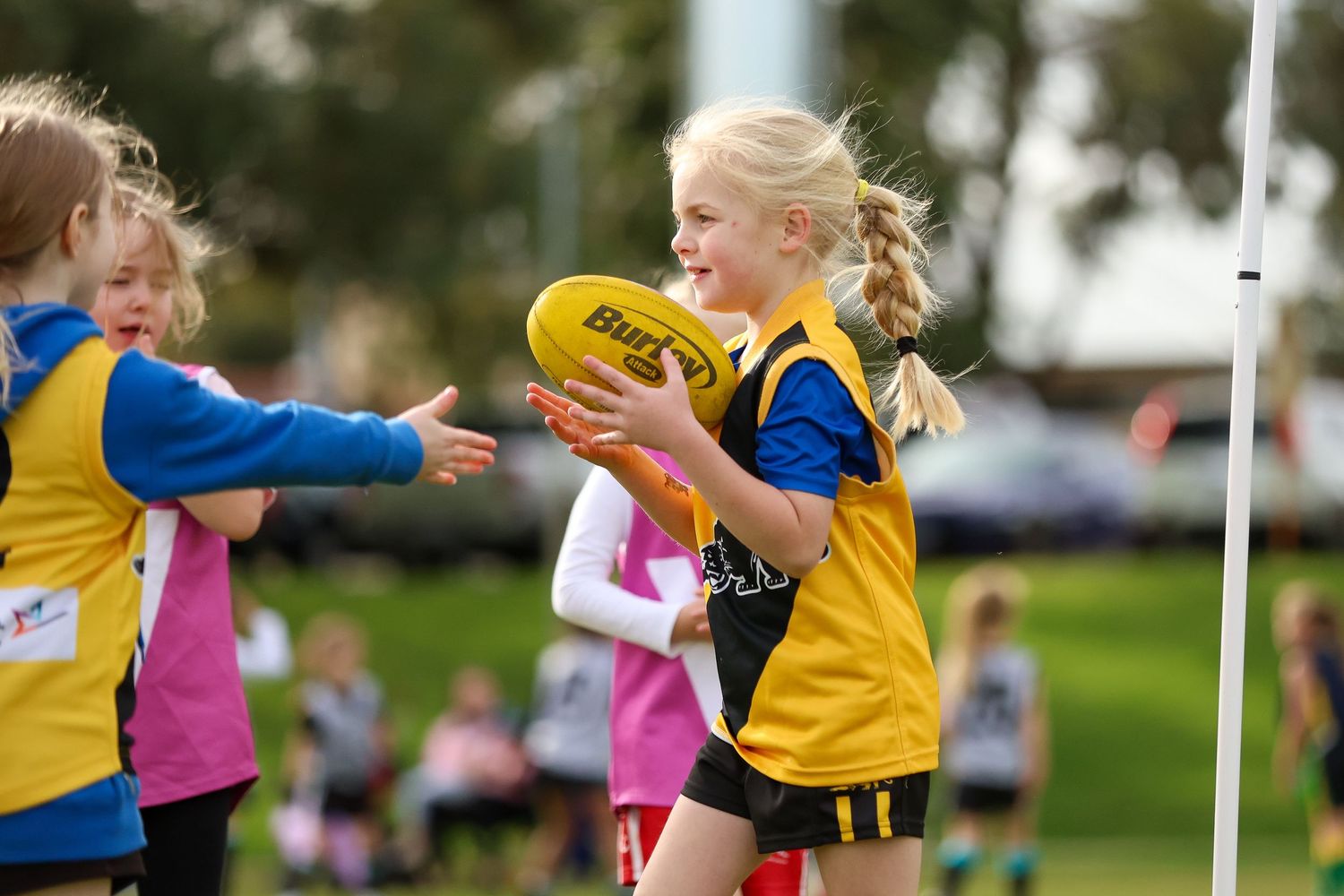 Kids in pink and yellow jerseys playing flag football compete for the ball during an outdoor game.