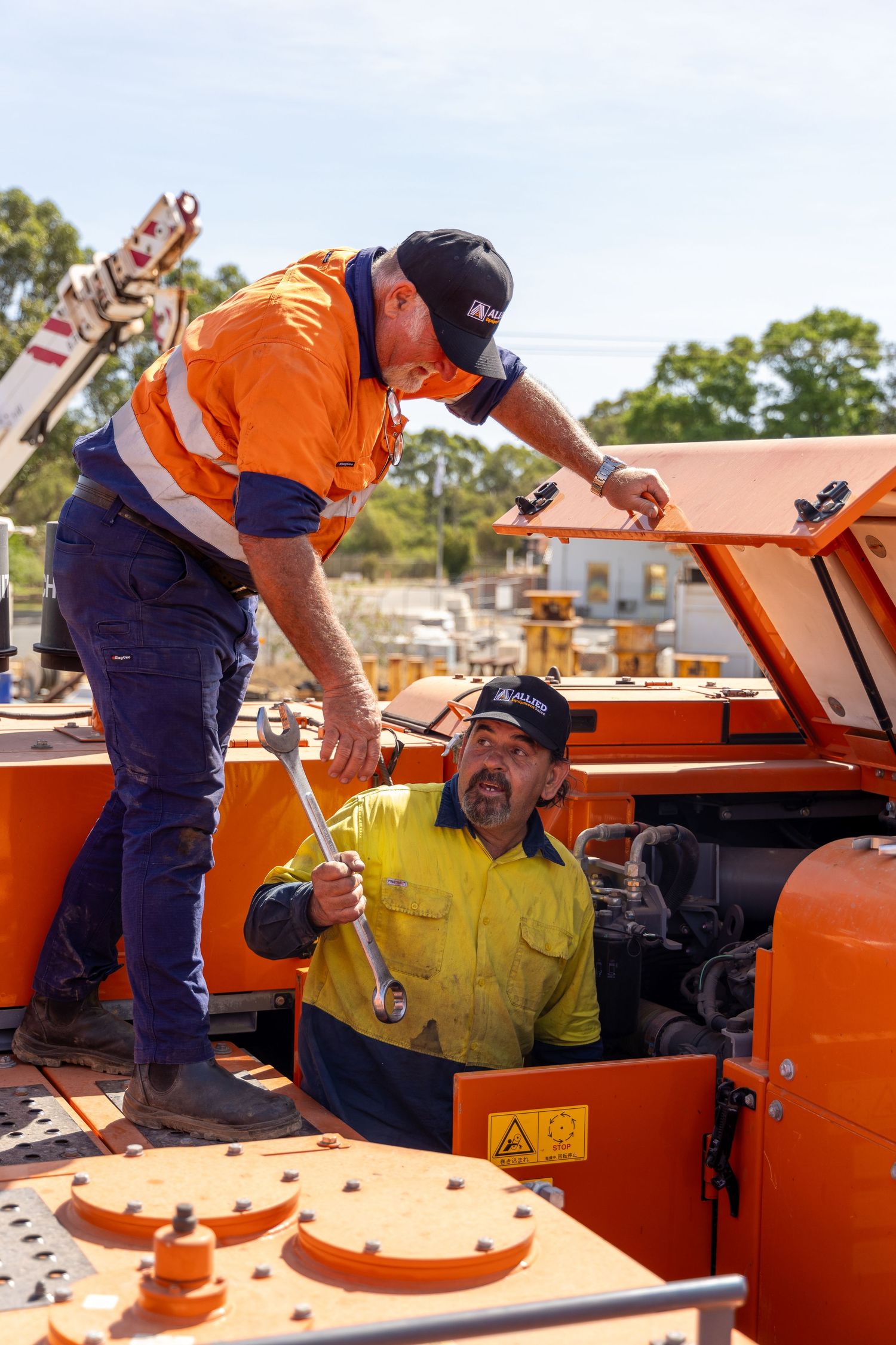 Industrial workers in hi-vis workwear collaborate on maintaining heavy equipment machinery outdoors.