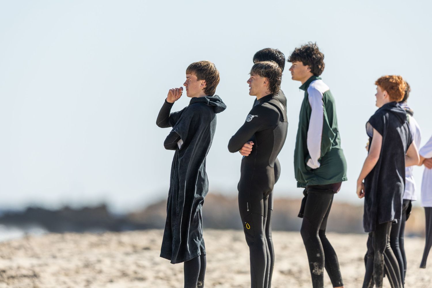 A sequence of people in wetsuits practicing surfing moves and stances on the beach.