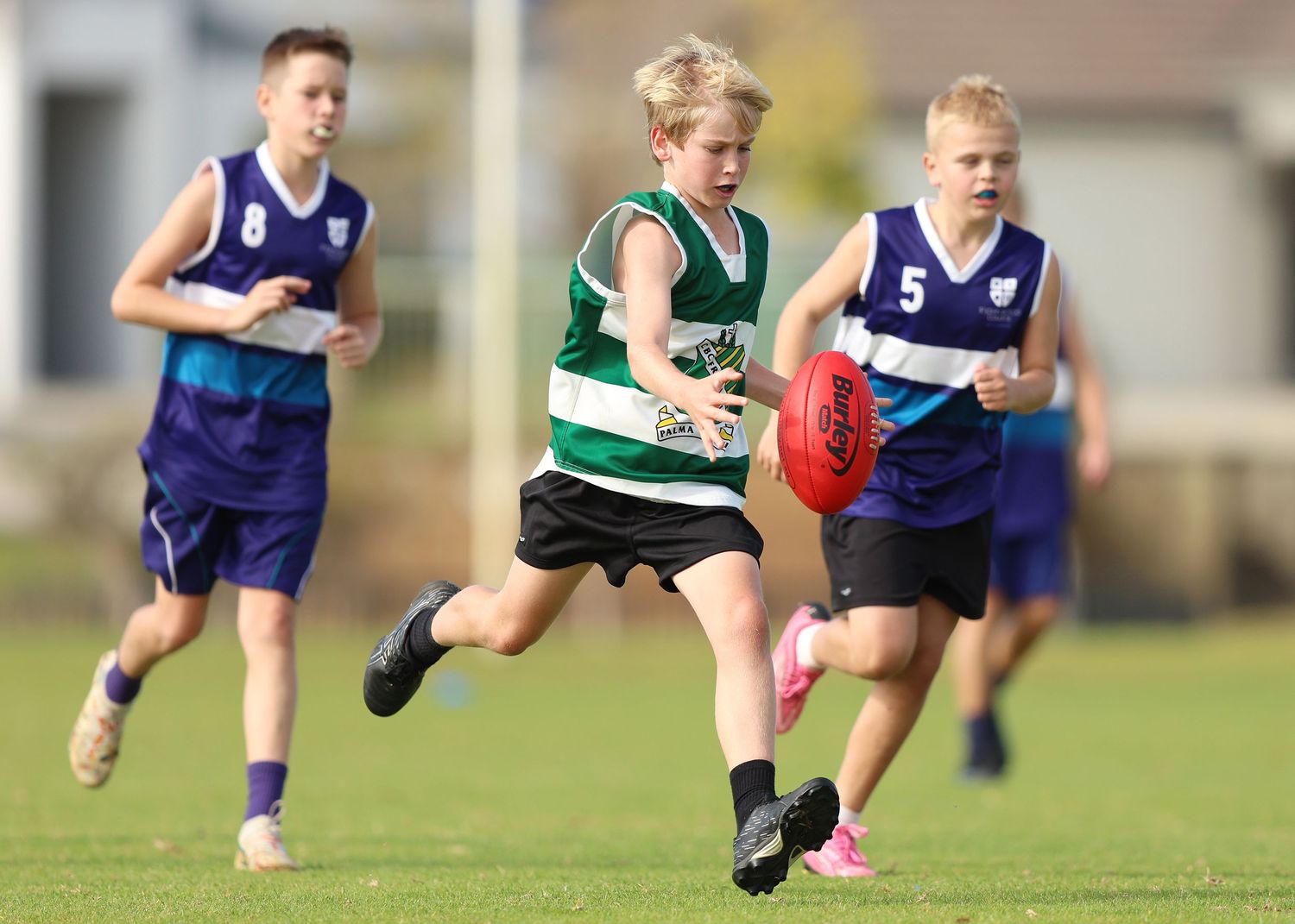 Youth rugby players tackle and dive for the ball during an intense match on a grass field.