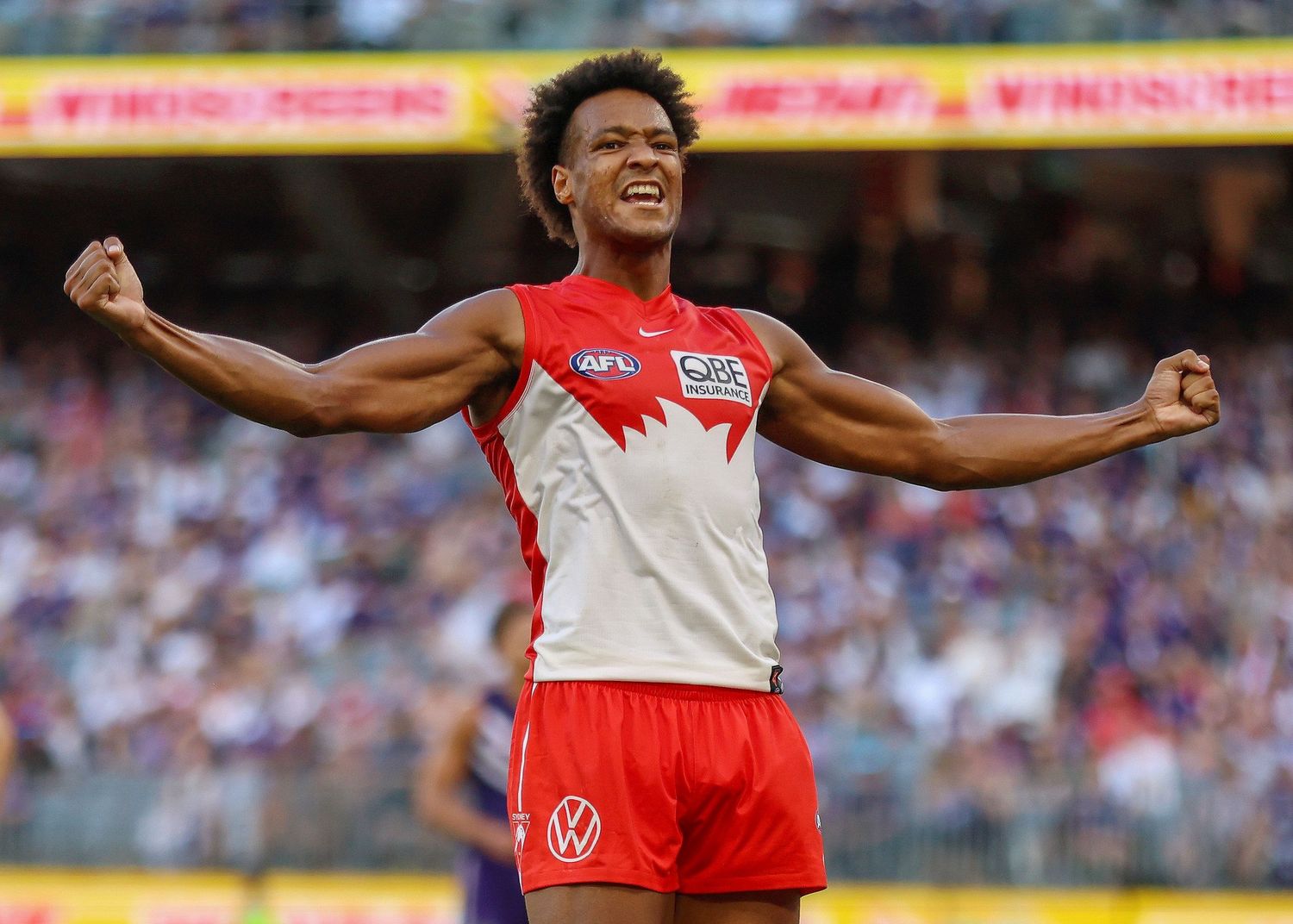 AFL player celebrates with arms outstretched wearing red and white uniform.