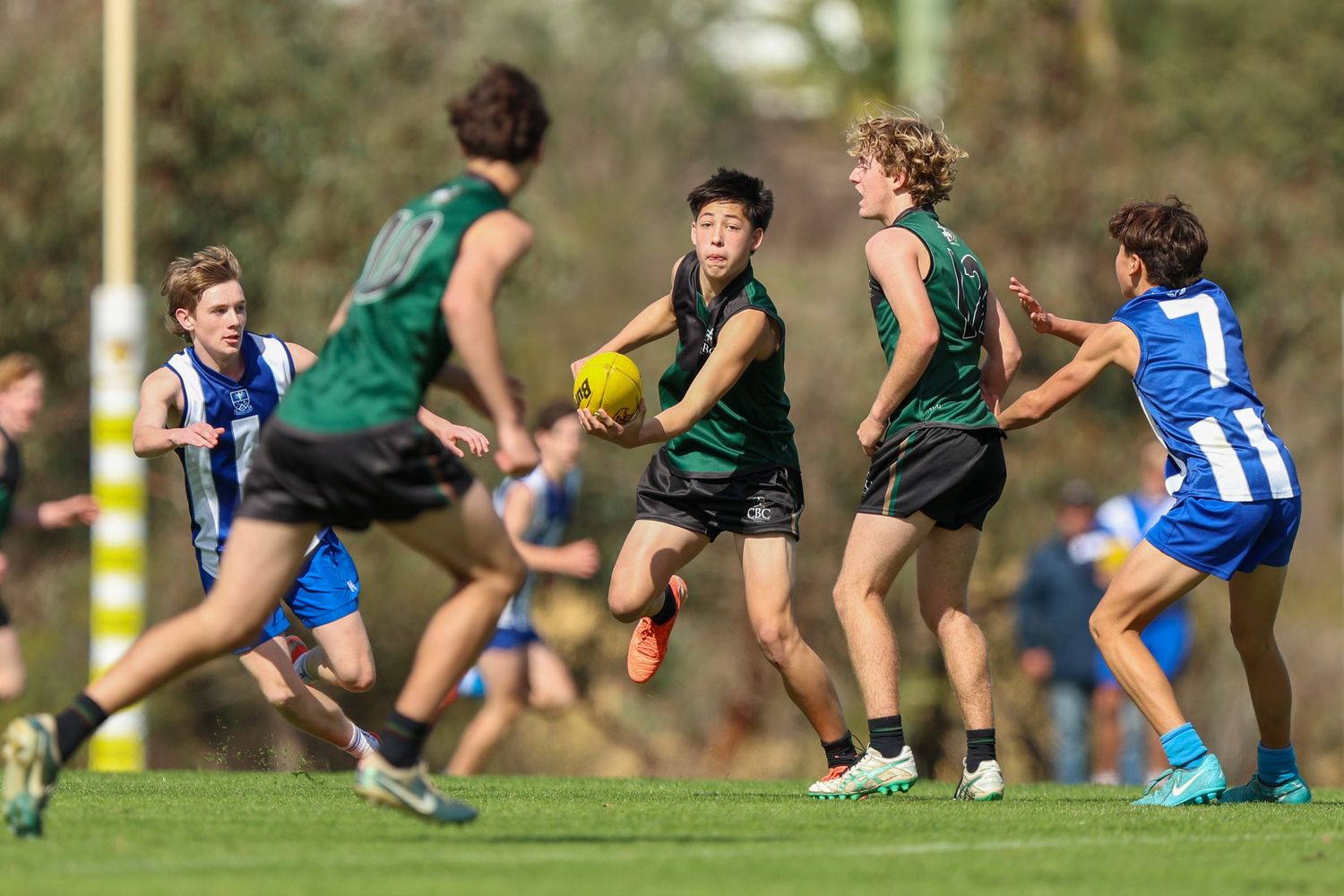 Australian football players in green and blue uniforms compete for possession during an intense match.