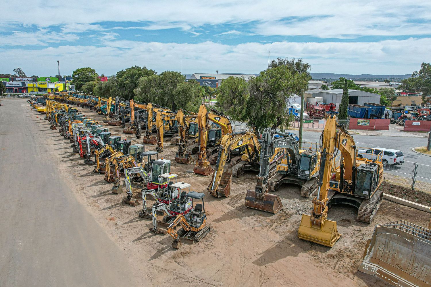 A long row of yellow construction equipment and excavators parked in a line at an outdoor heavy machinery lot.